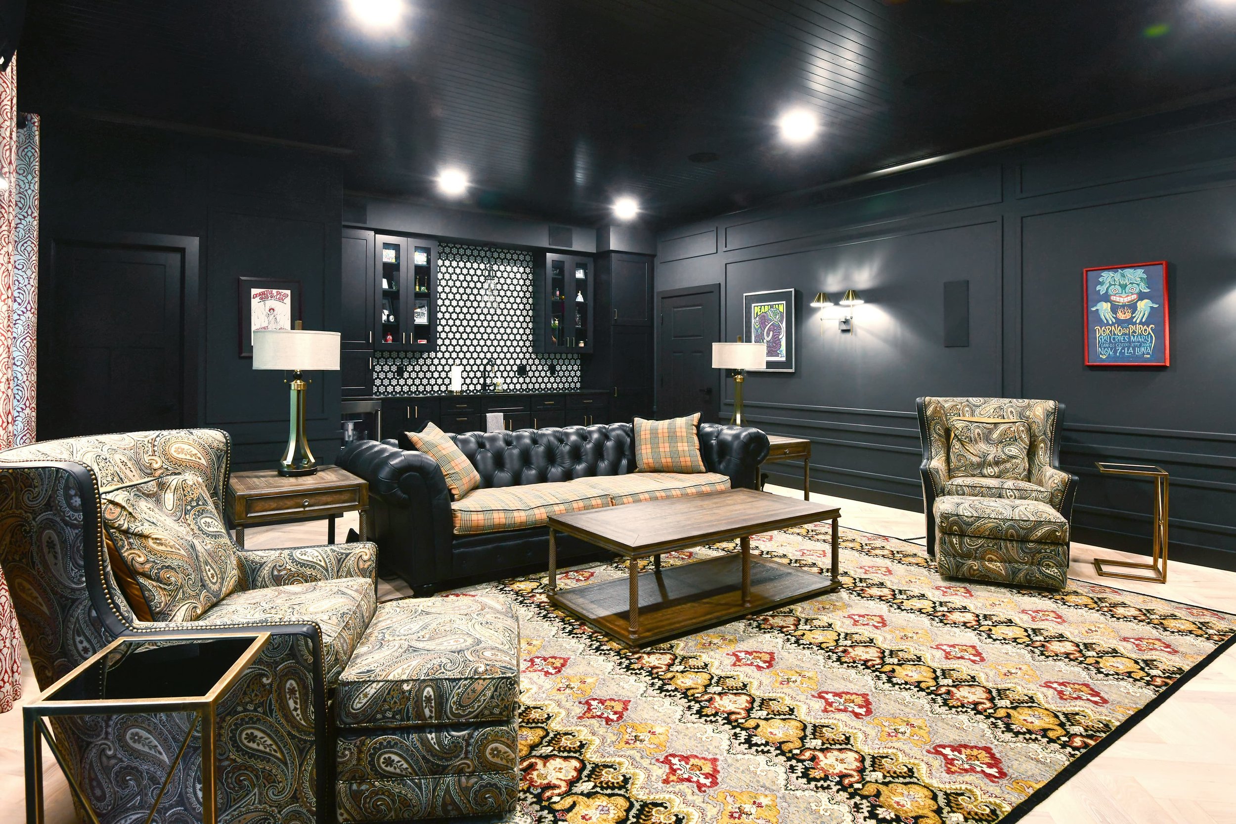 Moody living room interior design with custom upholstered seating, patterned area rug, and dark paneled walls, creating a refined, intimate gathering space in a Southwest Michigan home.