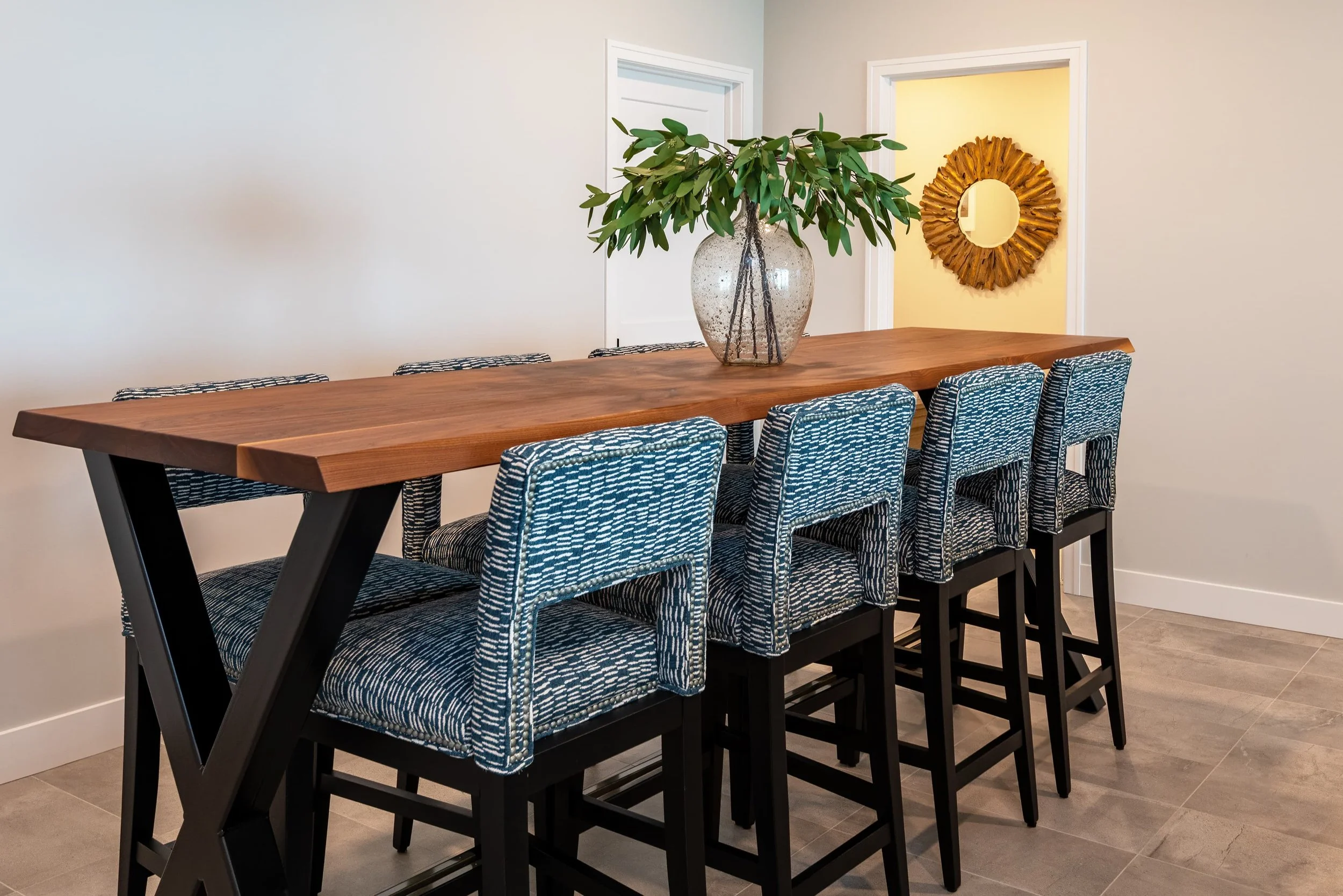 Dining area interior design featuring a custom wood table, upholstered counter-height seating, and warm natural accents, creating a refined, inviting gathering space in a Southwest Michigan home.