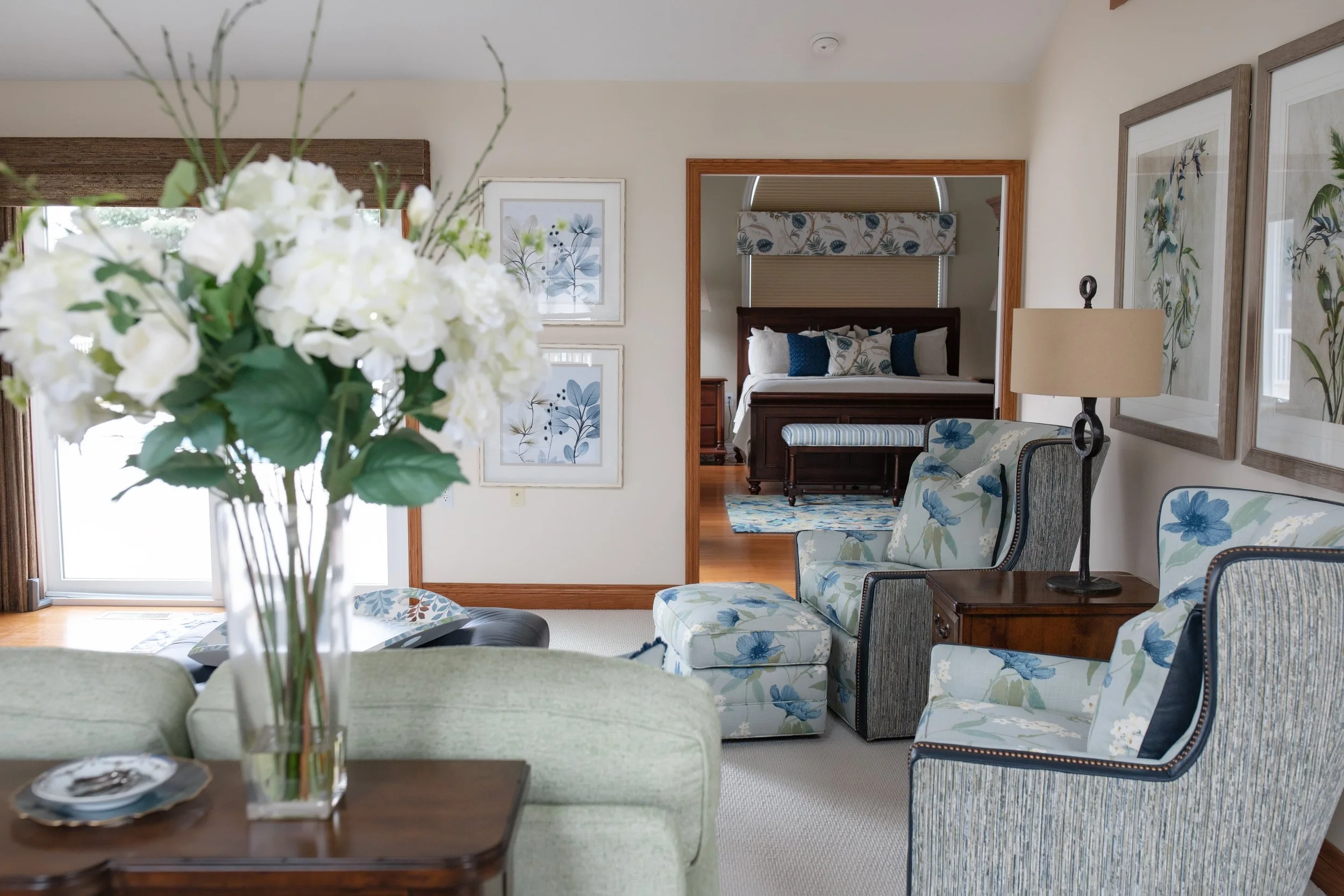 Serene sitting area with custom upholstered chairs, layered textiles, and coordinated bedroom design beyond, creating a calm, cohesive interior for lakeside living in Southwest Michigan.