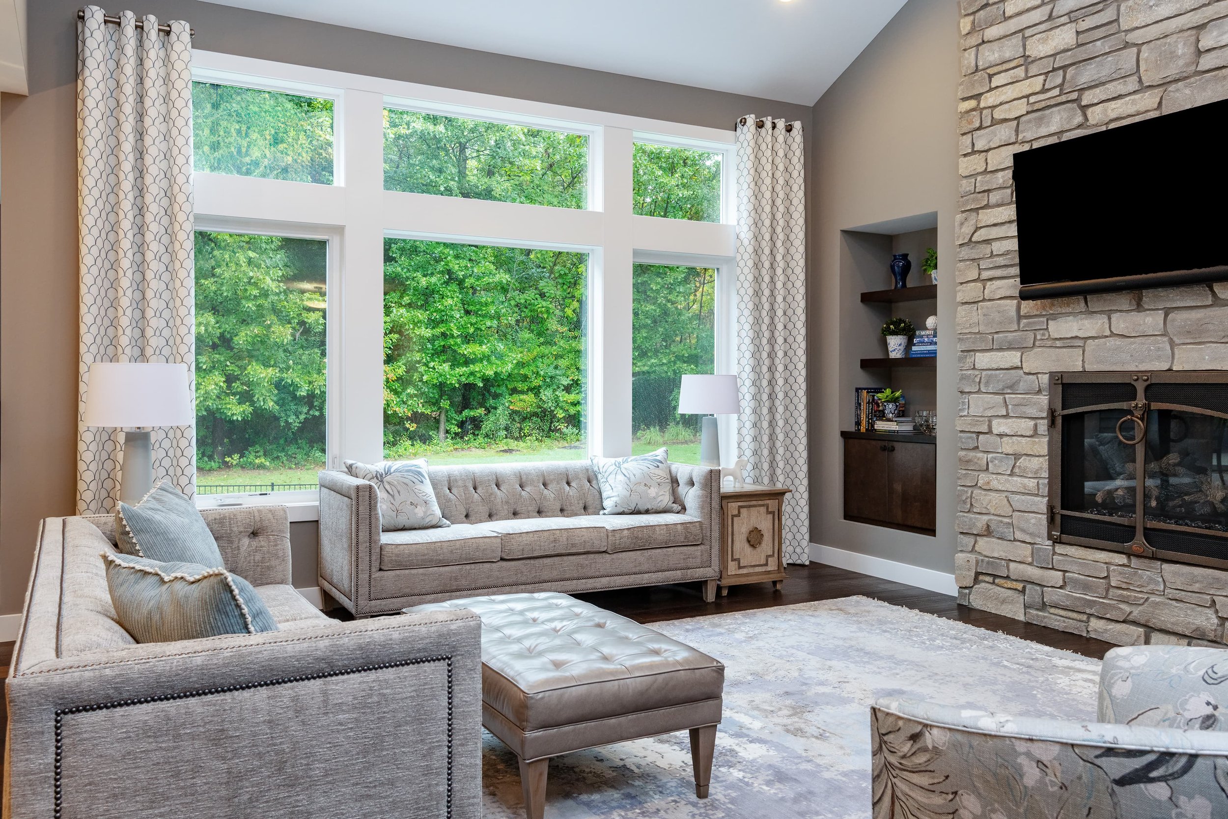 Living room interior design with custom upholstered seating, tailored window treatments, and a stone fireplace, creating a warm, light-filled gathering space in a Southwest Michigan home.