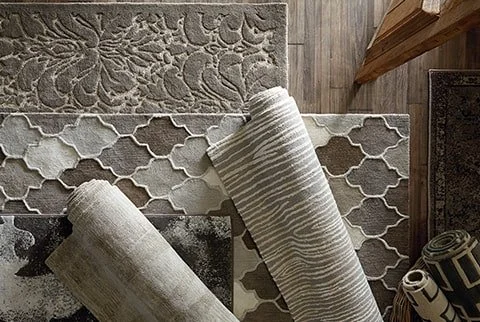 Several rolled-up rugs and multiple installed rugs on the floor with various patterns and textures.