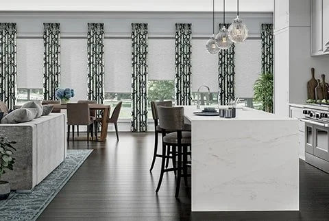 Modern open-concept living and kitchen area with a white island, dark bar stools, dining table, patterned curtains, and pendant lighting.