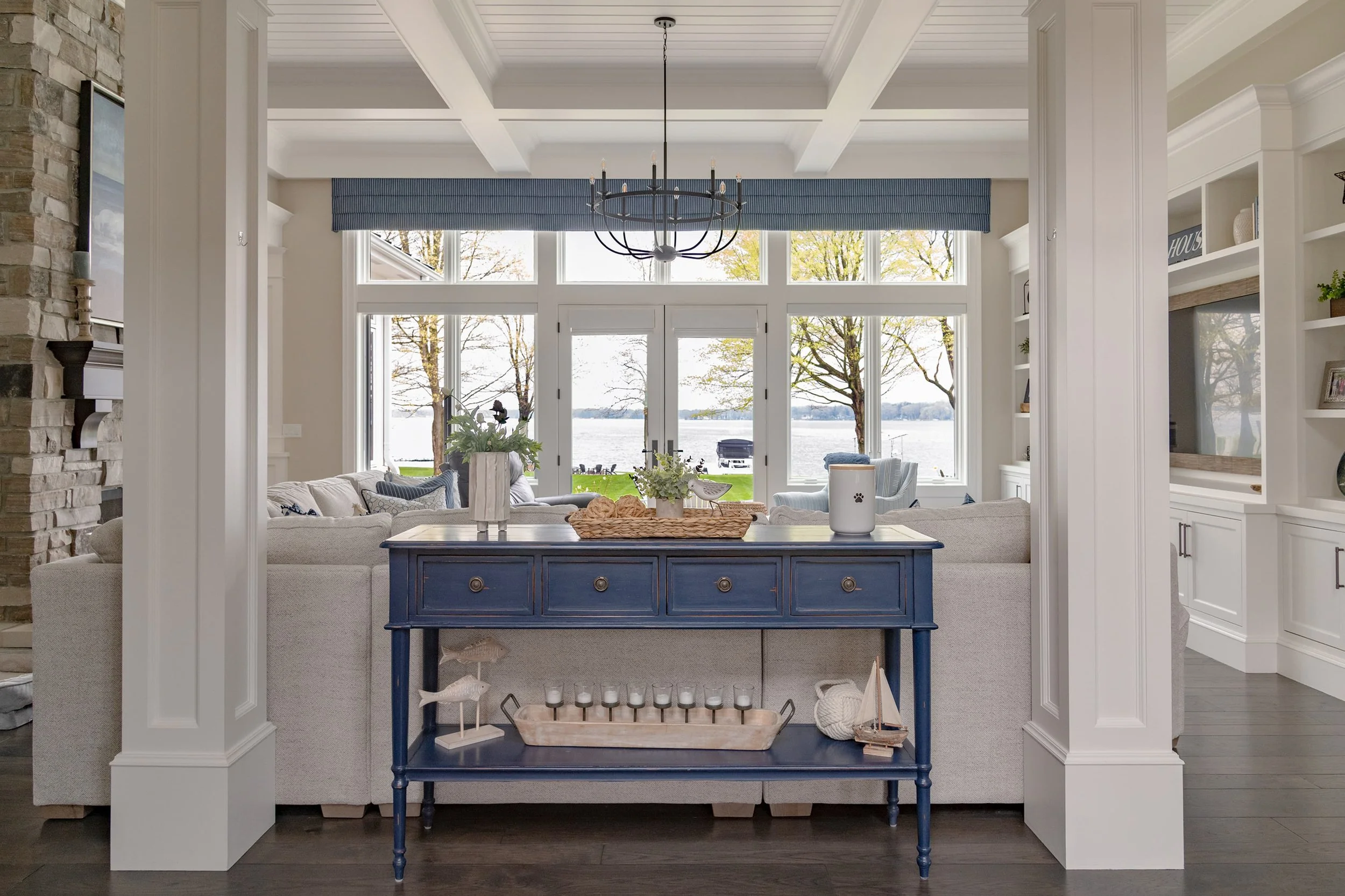Lakeside living room interior design with custom furnishings, coffered ceiling, tailored window treatments, and expansive lake views, creating a calm, welcoming home in Southwest Michigan.