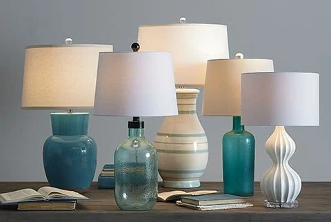 Six table lamps with shades and vases in various shapes and sizes on a wooden surface.