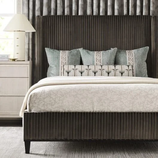 A bedroom with a bed, beige and gray pillows, beige bedding, two matching lamps, and framed botanical artwork on the wall.