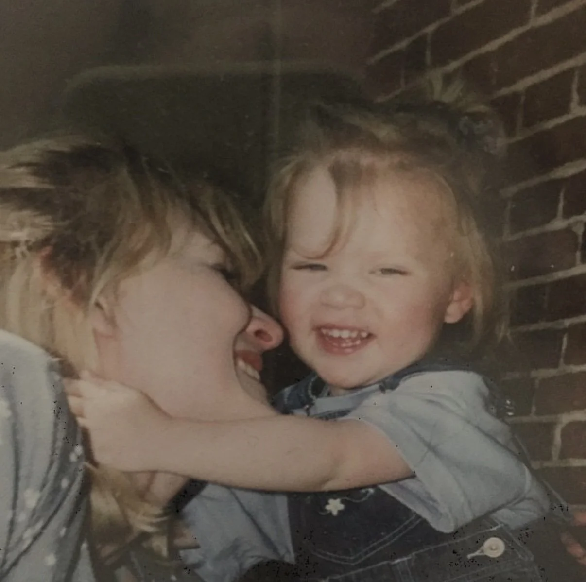 A woman and a young child sharing a joyful moment, with the woman kissing the child on the cheek and the child laughing.