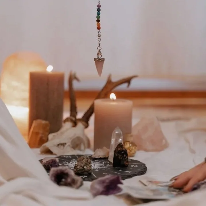 Bohemian-style altar with candles, crystals, rocks, and hanging pendulum, decorated with candles, gemstones, and driftwood.