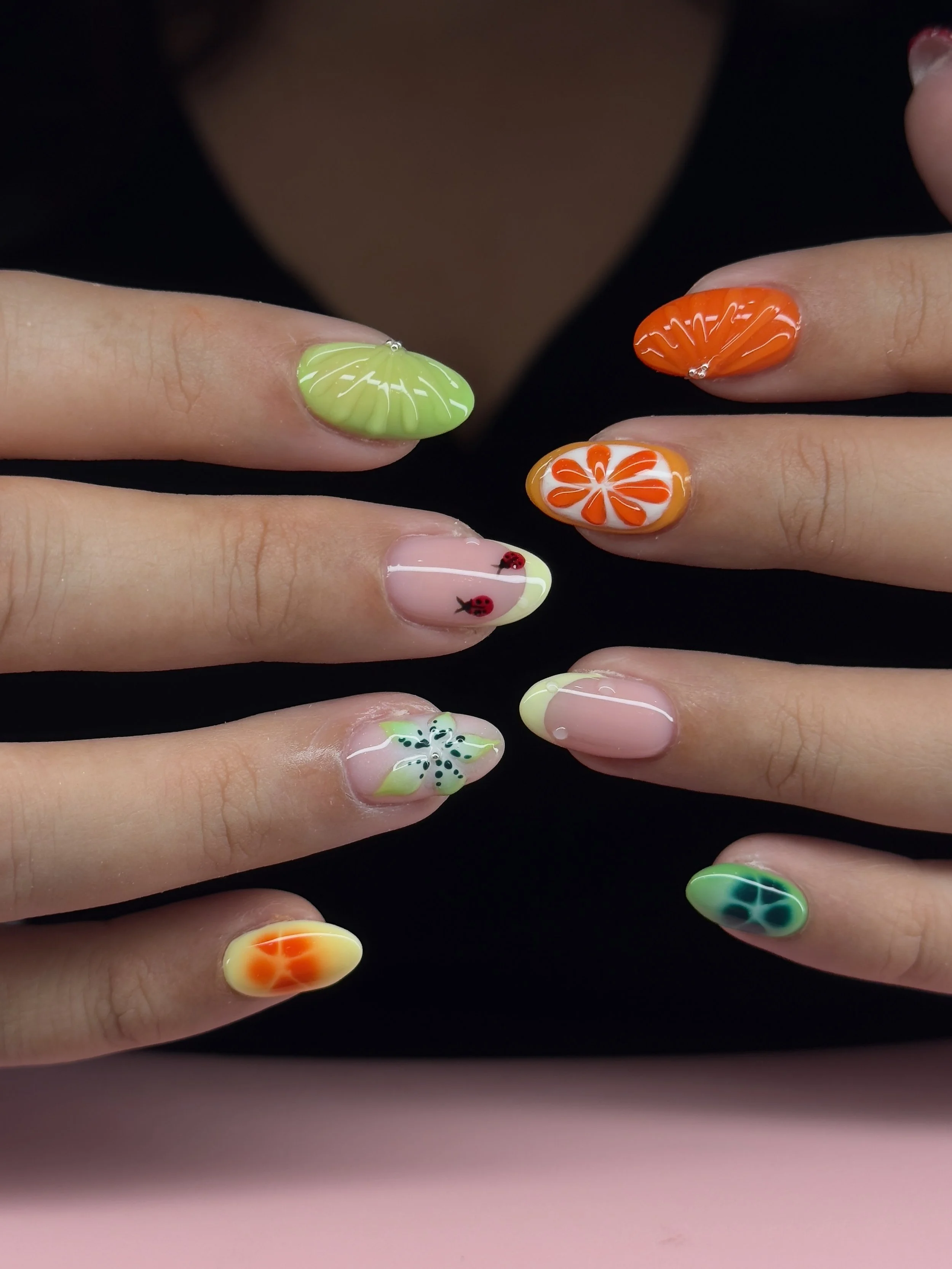 Close-up of hands with colorful floral and fruit-themed nail art on fingernails.