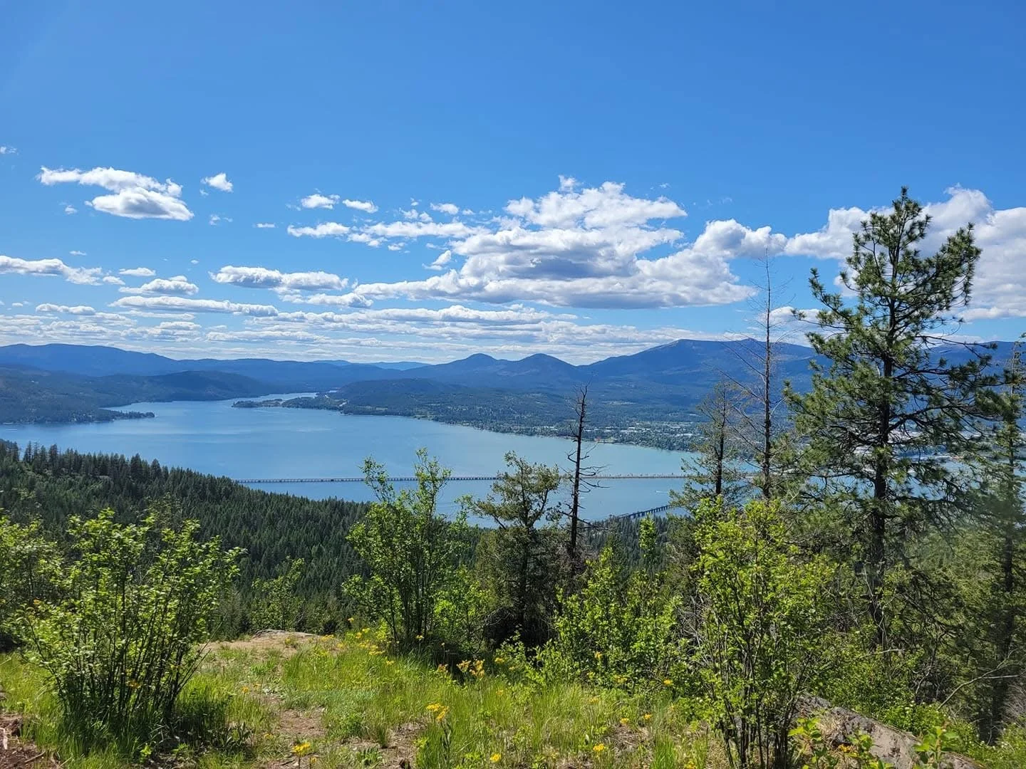 Scenic view of a large lake surrounded by forested hills and mountains under a partly cloudy sky.