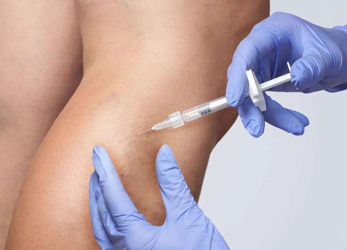 A person wearing medical gloves administering a vaccine or injection into their thigh.