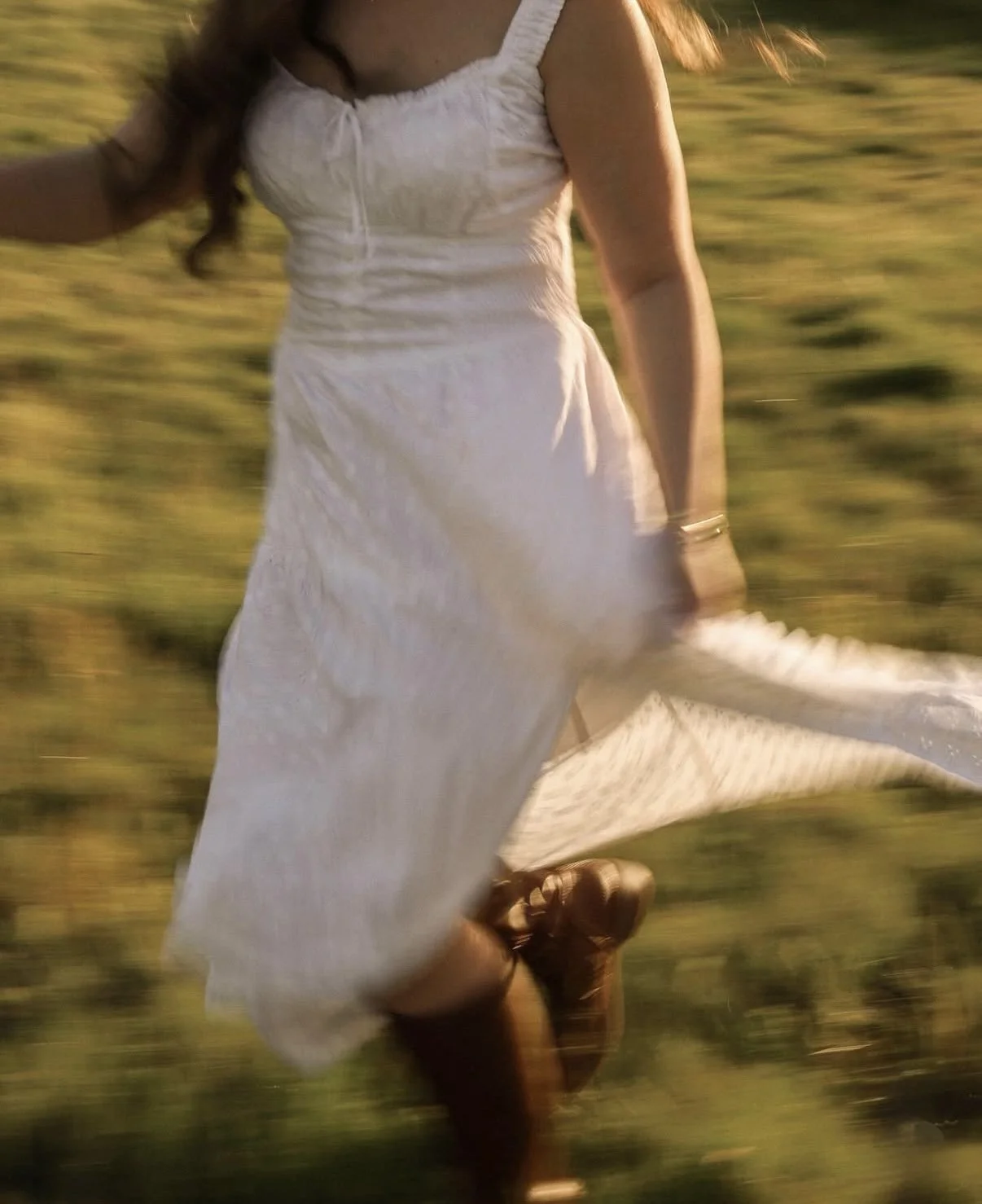 A person in a white dress running through a grassy field during sunset.
