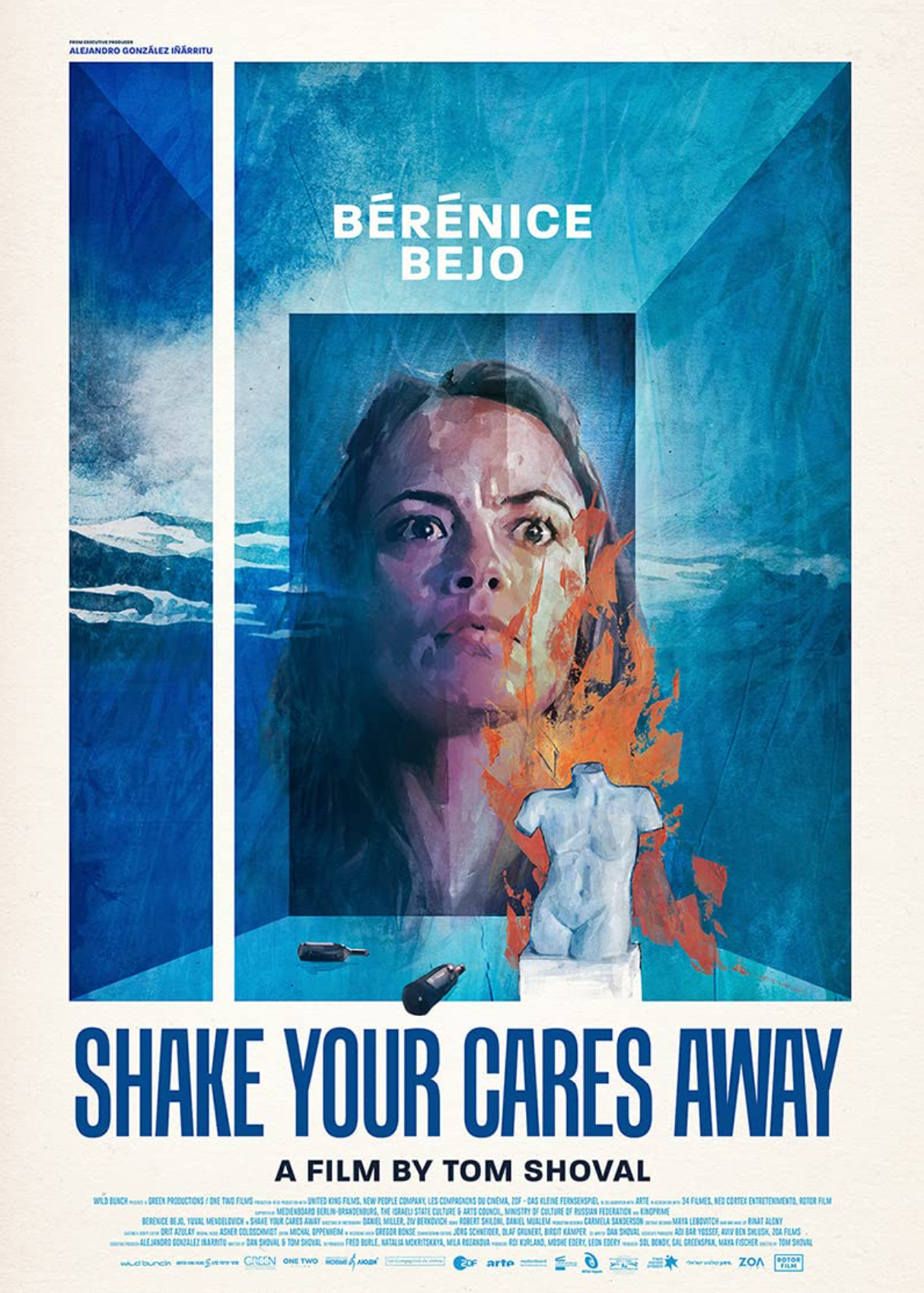 A movie poster for the film 'Shake Your Cares Away' directed by Tom Shoval. It features a portrait of a woman with a surprised expression, with mountains and sky in the background. There is a small sculpture of a torso and a bottle on a table in front of her, with flames and a shoe also depicted. The title is in large blue letters at the bottom of the poster.