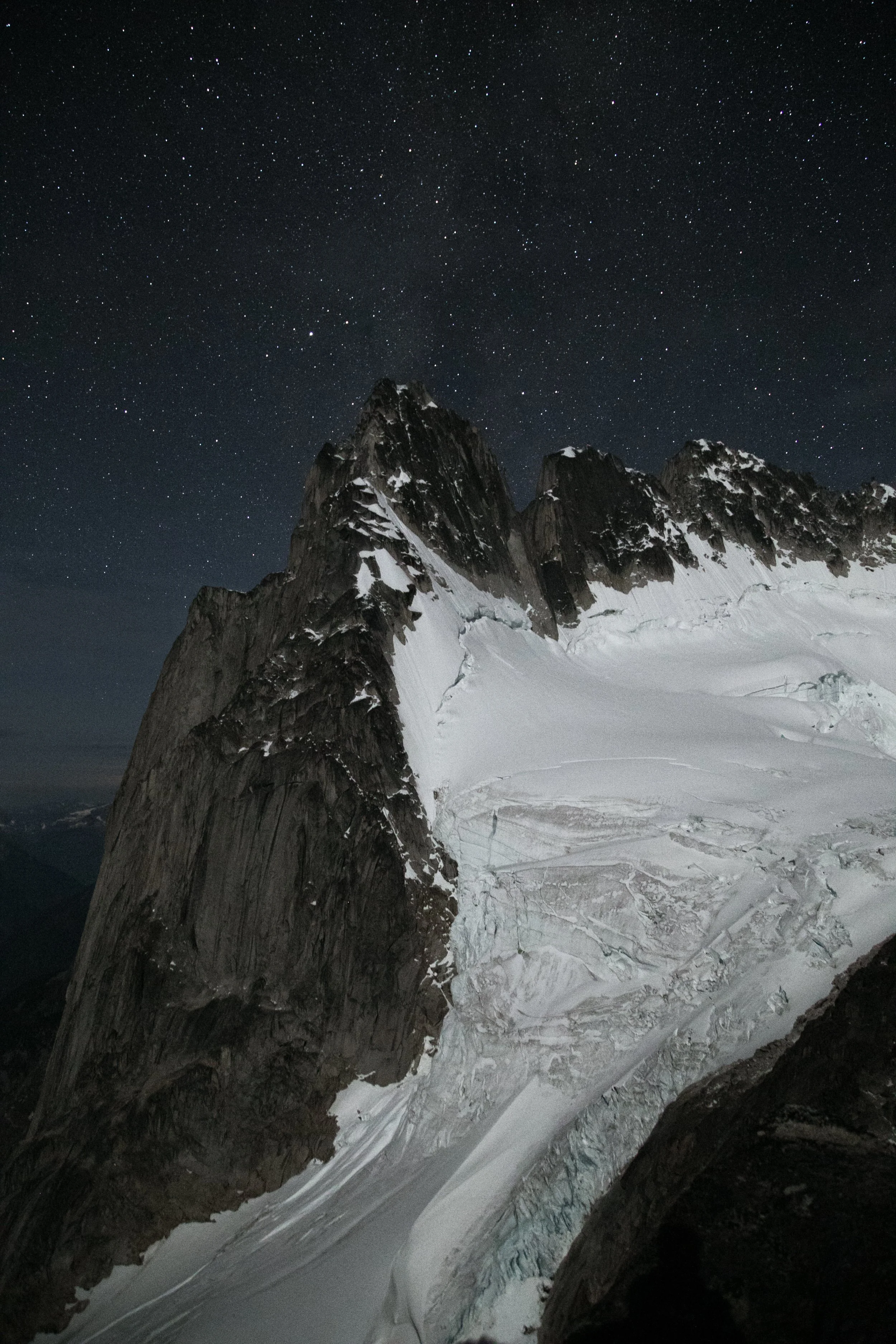 Nighttime view of snow-covered mountain peaks and glaciers under a star-filled sky.