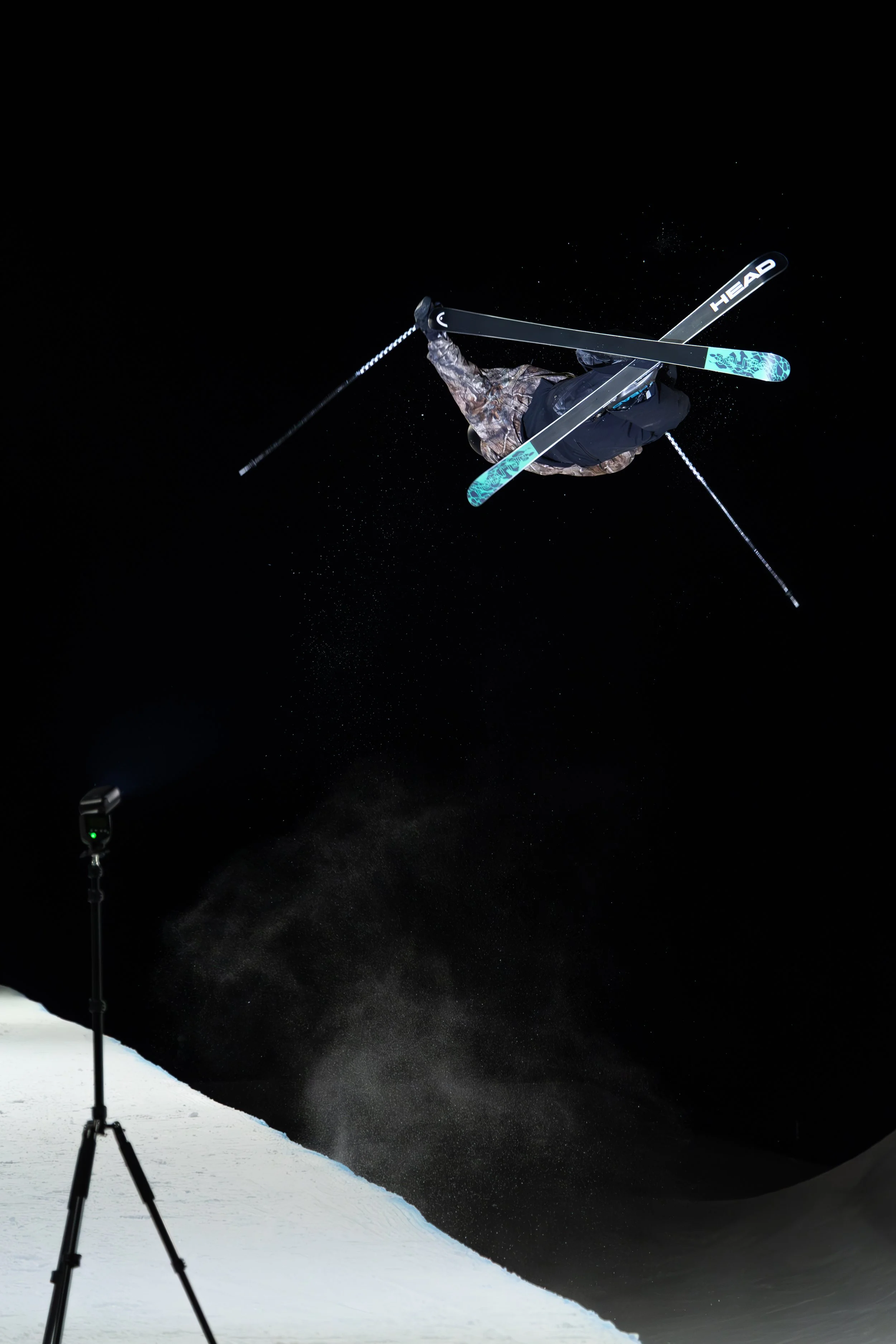 A skier performing an aerial trick at night on snow with a flash or light illuminating the scene.