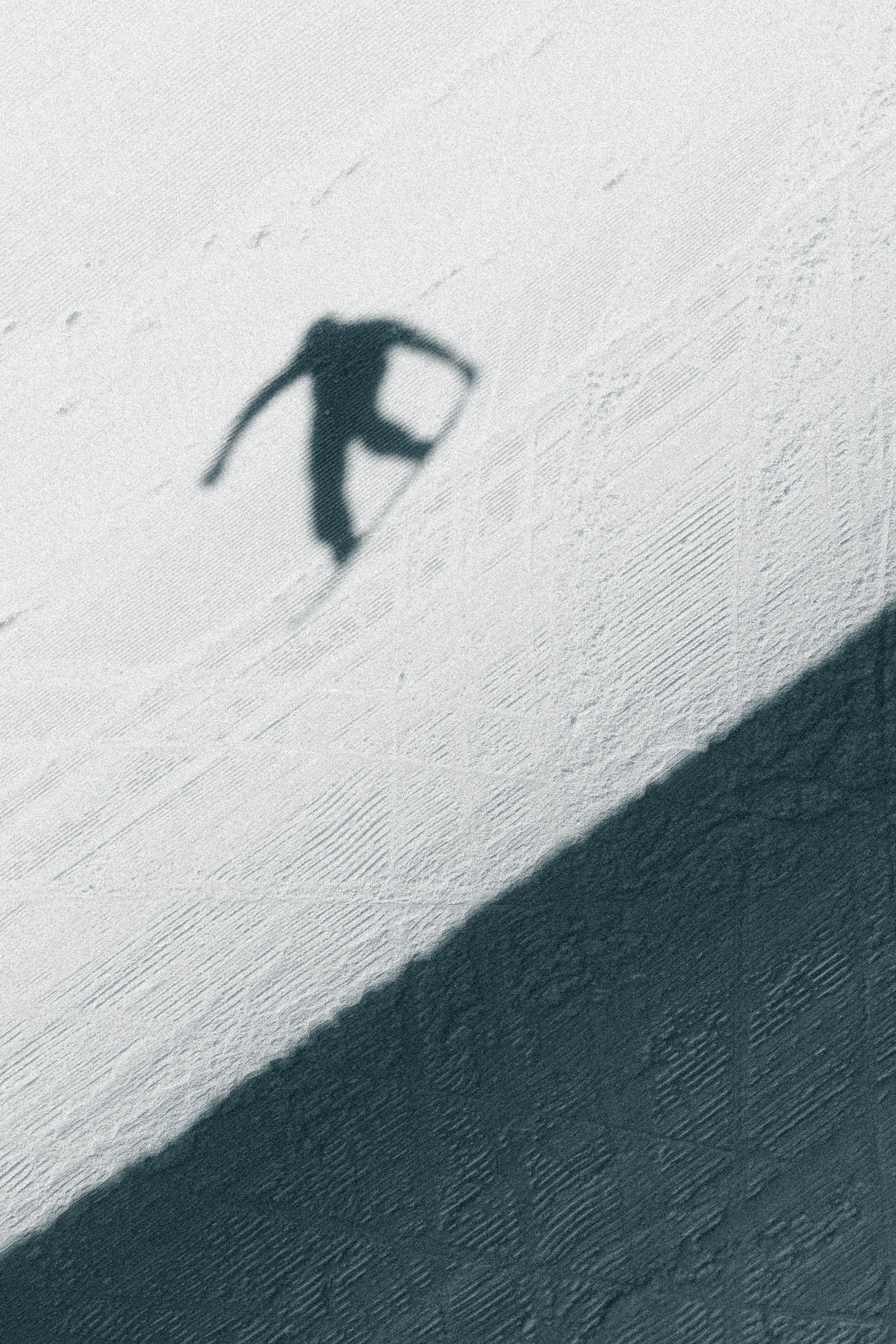 Shadow of a person skating on the snow with a backpack, with snow and textured ground visible.