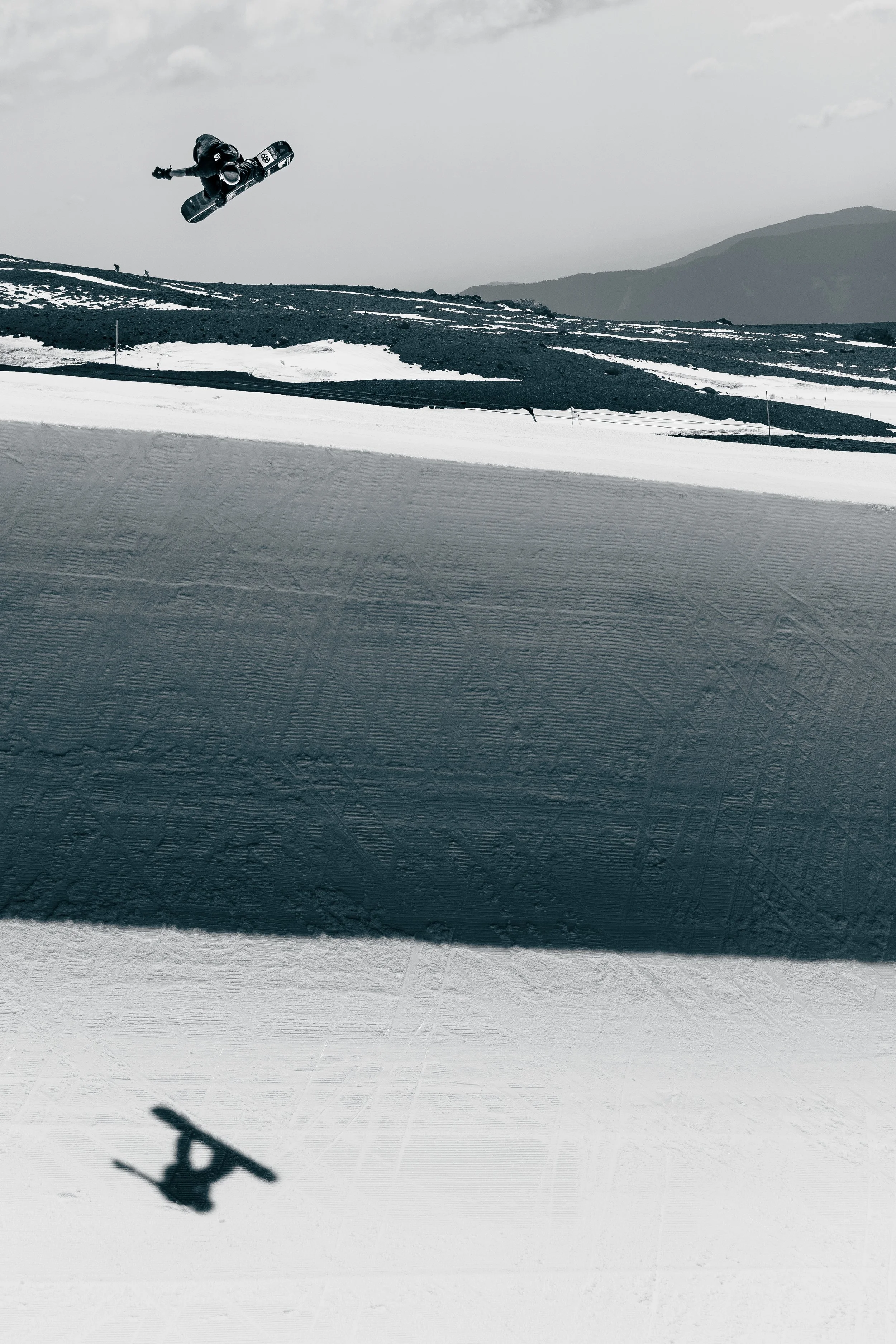 A skier in mid-air performing a trick above a snowy slope with mountains in the background.