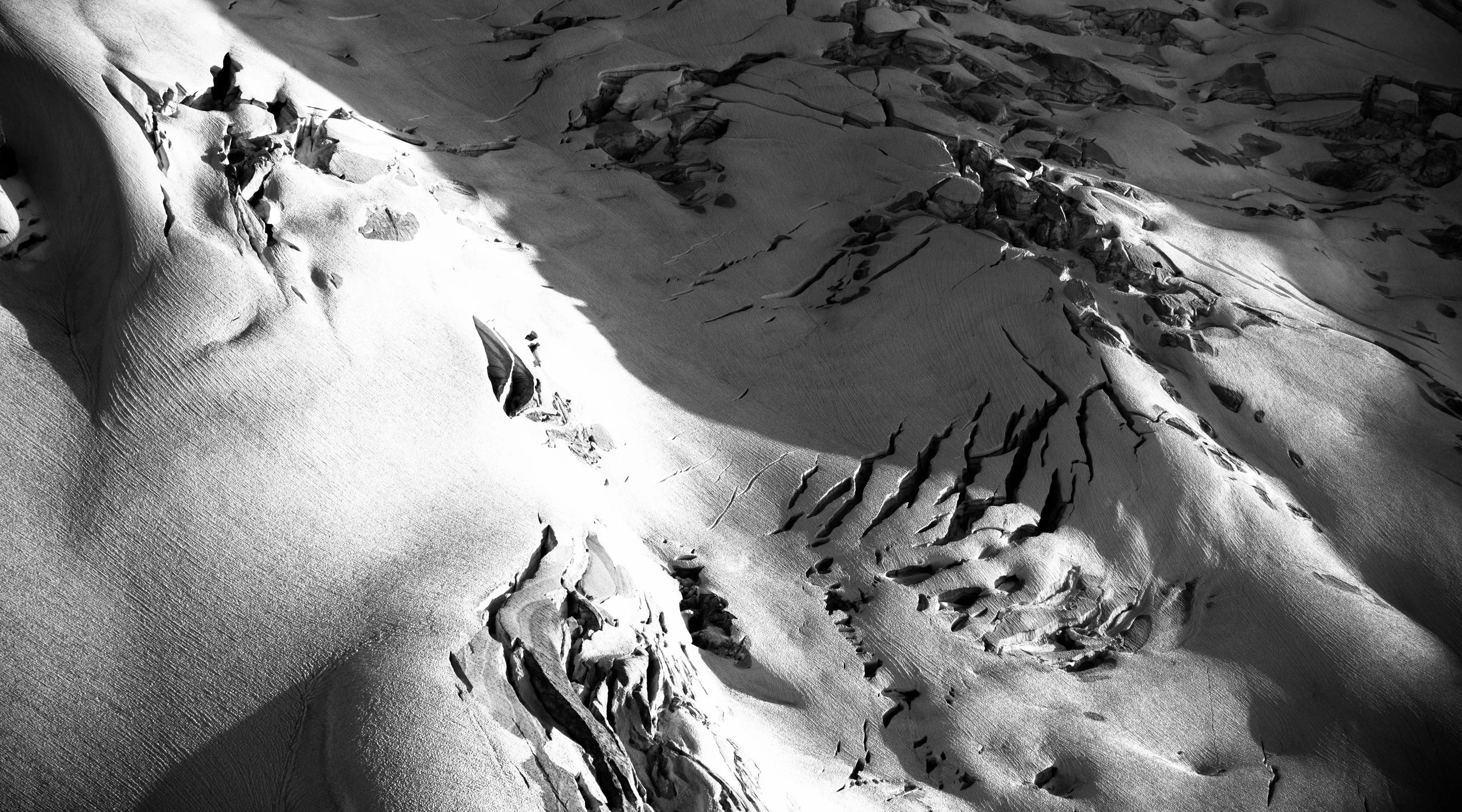 Snow-covered mountain slope with deep cracks and rocky outcroppings in black and white