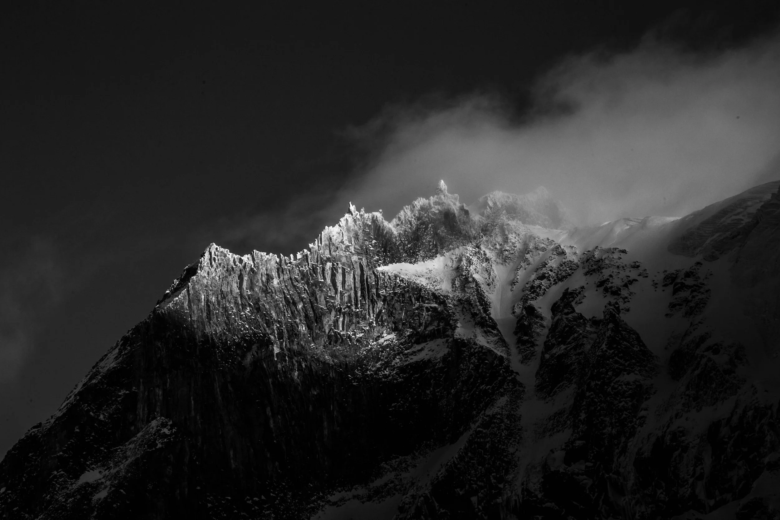 Snow-covered mountain peak with dramatic clouds in the sky.