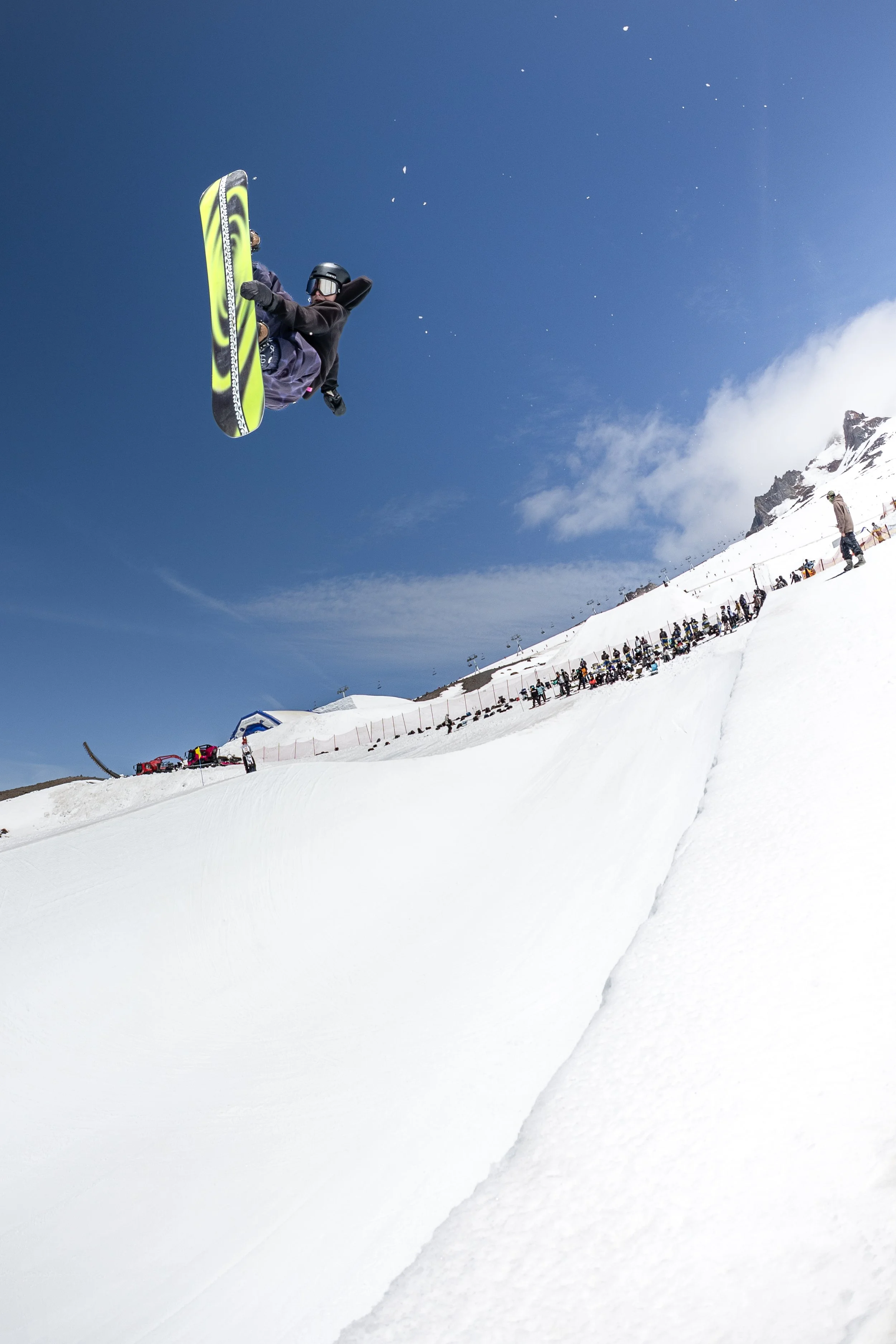 Skier performing a jump off a snow ramp on a clear, sunny day at a ski resort.