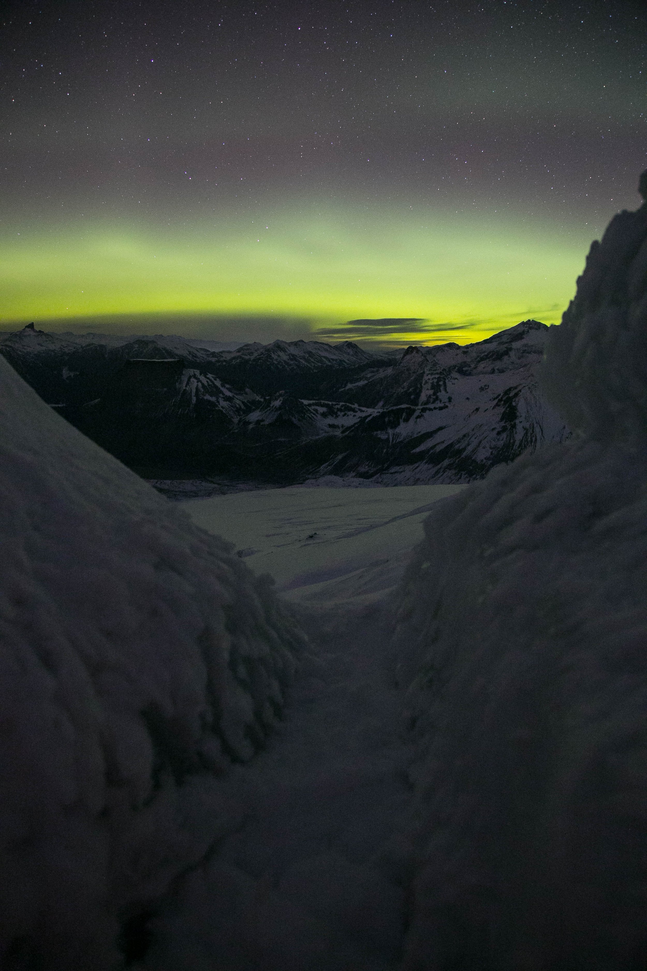 Night sky with visible stars and the northern lights over snow-covered mountain landscape.
