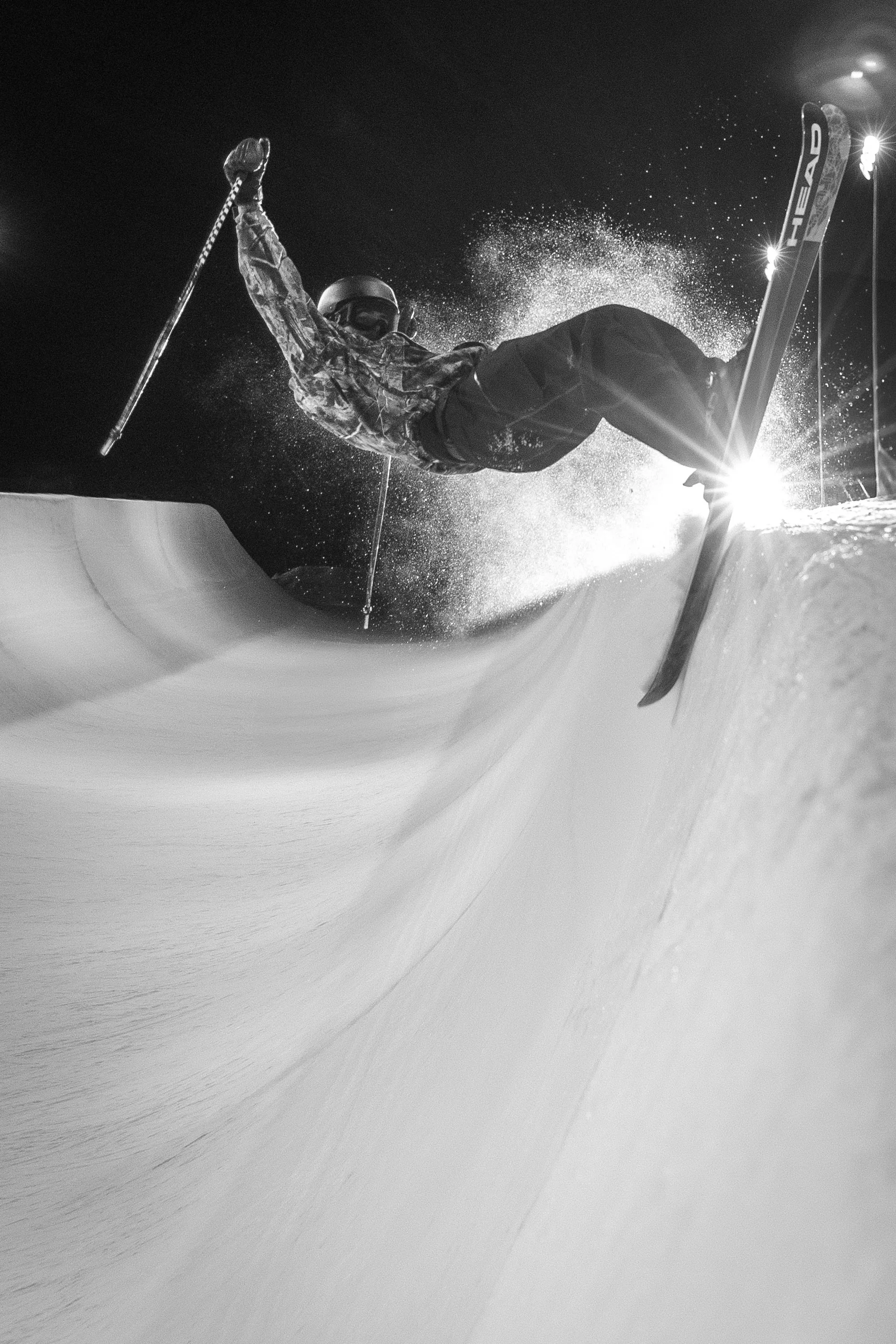 Nighttime snowboarding scene with a person mid-air performing a trick on a snow ramp, illuminated by stadium lights.