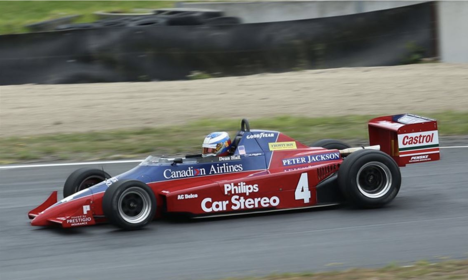 A vintage IndyCar race car with the number 4, colored red and blue, speeding on a racetrack with sponsorship decals, including Canadian Airlines and Castrol.