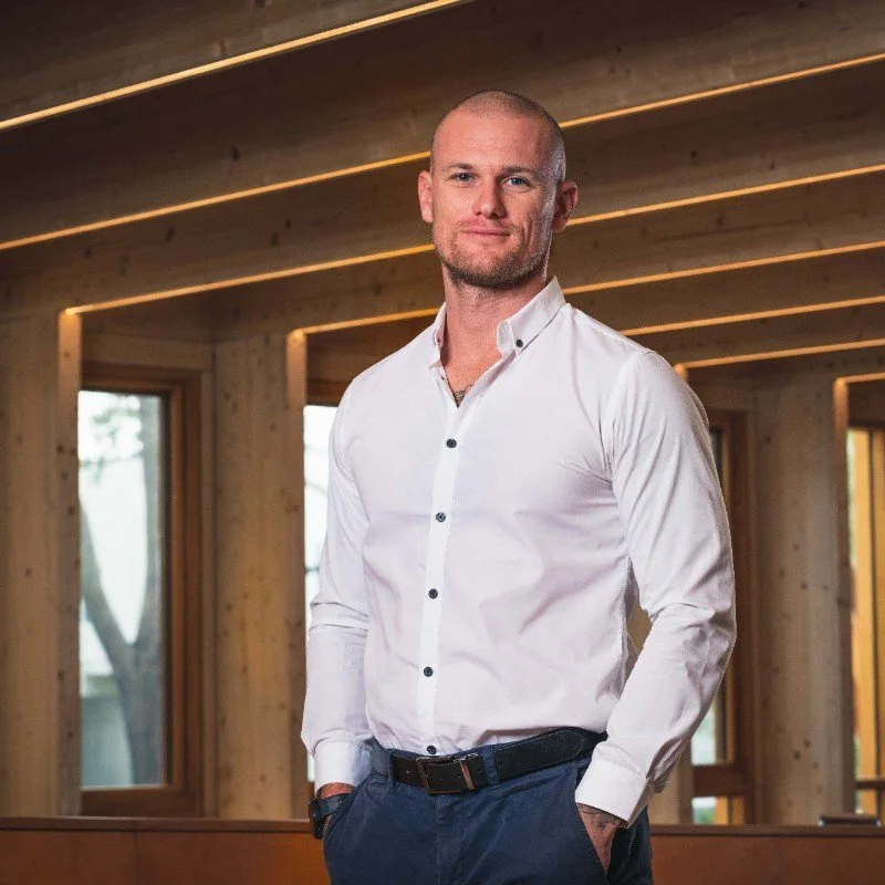 A tall handsome man who looks like he may have been a cold blooded killer in a previous life, perfectly filling out a classy white business shirt, looking square down the barrel of the camera with an alluring Brad Pitt like stare.