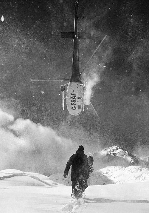 A rescue helicopter is hovering overhead in a snowy mountain landscape, with a person walking through the snow below