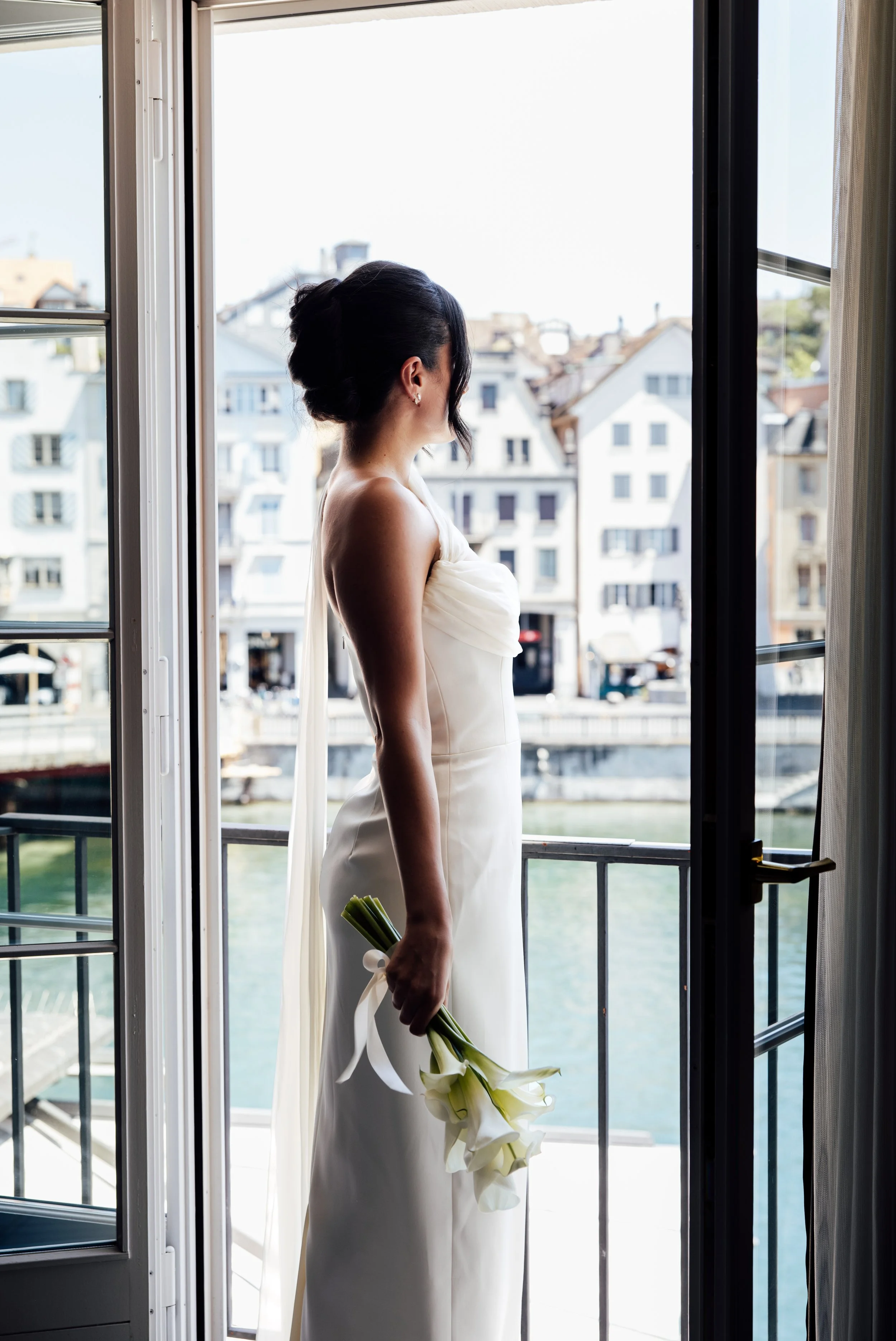 Von hinten am offenen Balkonfenster: die Braut mit Callas, dahinter Altstadthäuser am Fluss