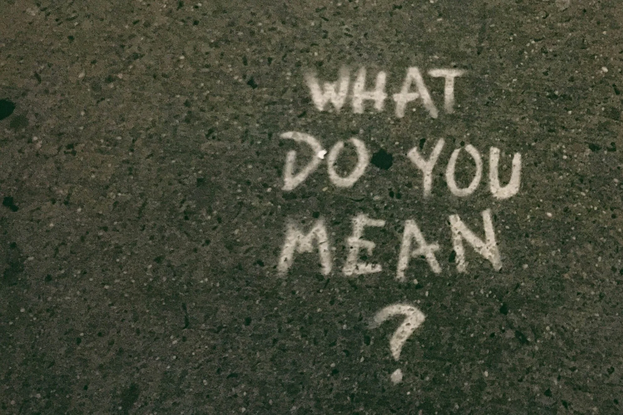 The words "What do you mean?" written in white chalk on concrete path
