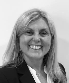 Black and white photo of a woman with blonde hair smiling, wearing a dark blazer and a white blouse.