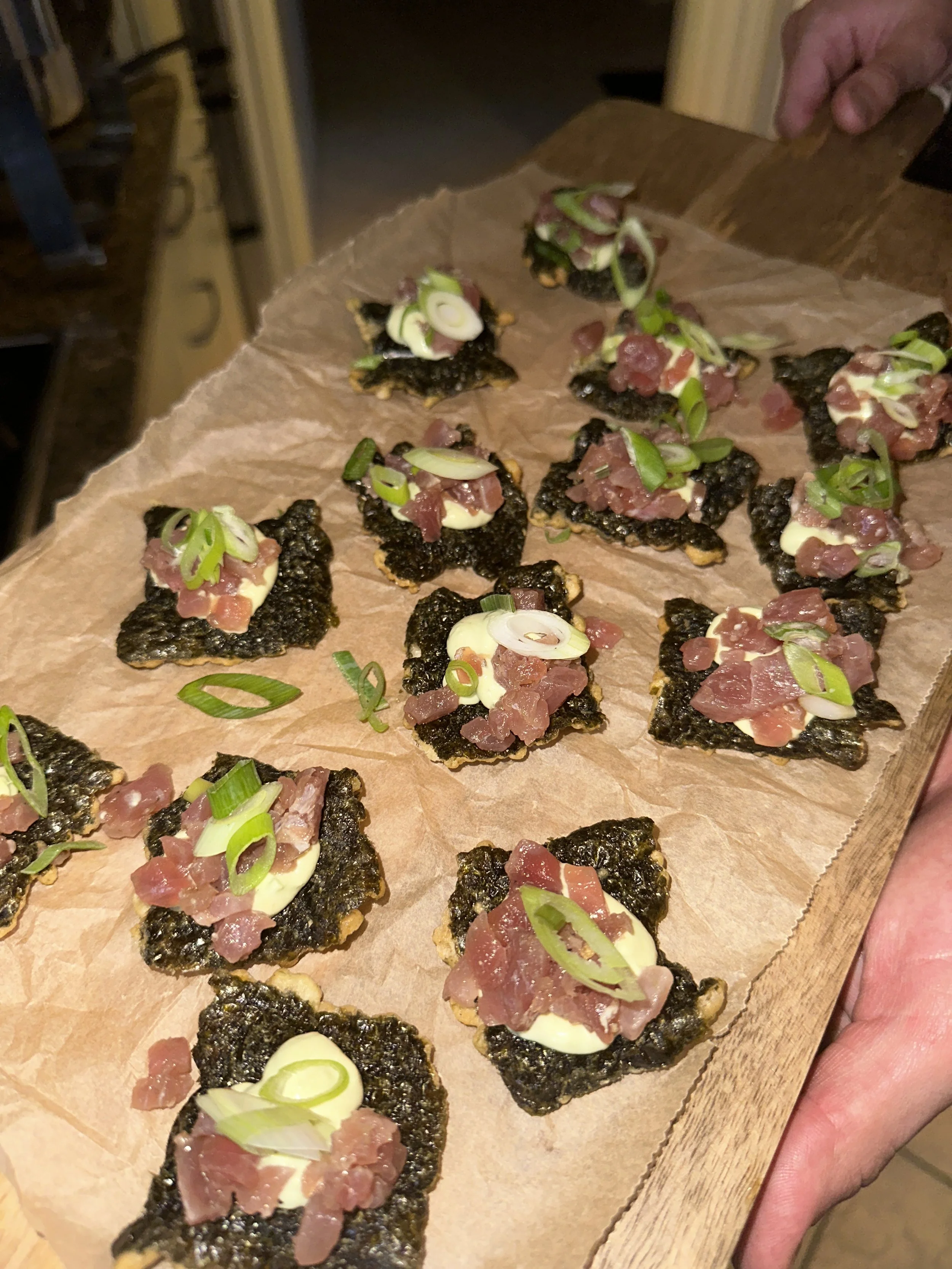 Kleine porties met zeewier, mayonaise, tonijn, en groene ui op een houten plank.