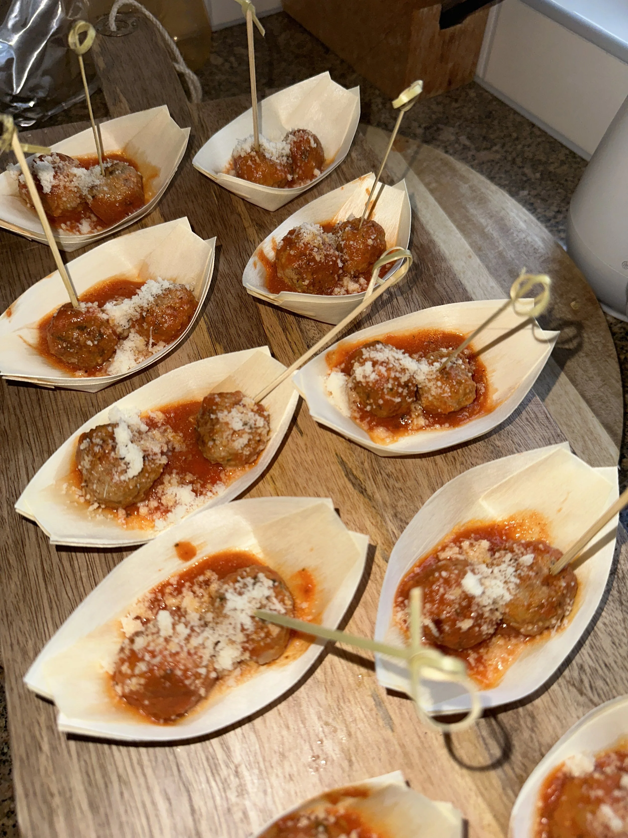 Mini Italiaanse gehaktballetjes in tomatensaus geserveerd in papieren bootjes met parmezaanse kaas.