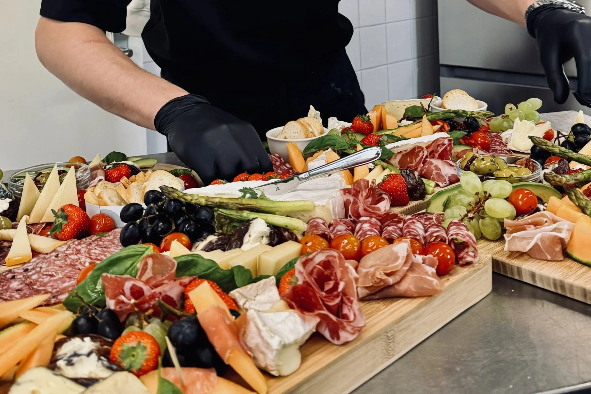 Diverse soorten kaas, vleeswaren, druiven, aardbeien, cherrytomaten, groenten en crackers op een houten kaasplank.