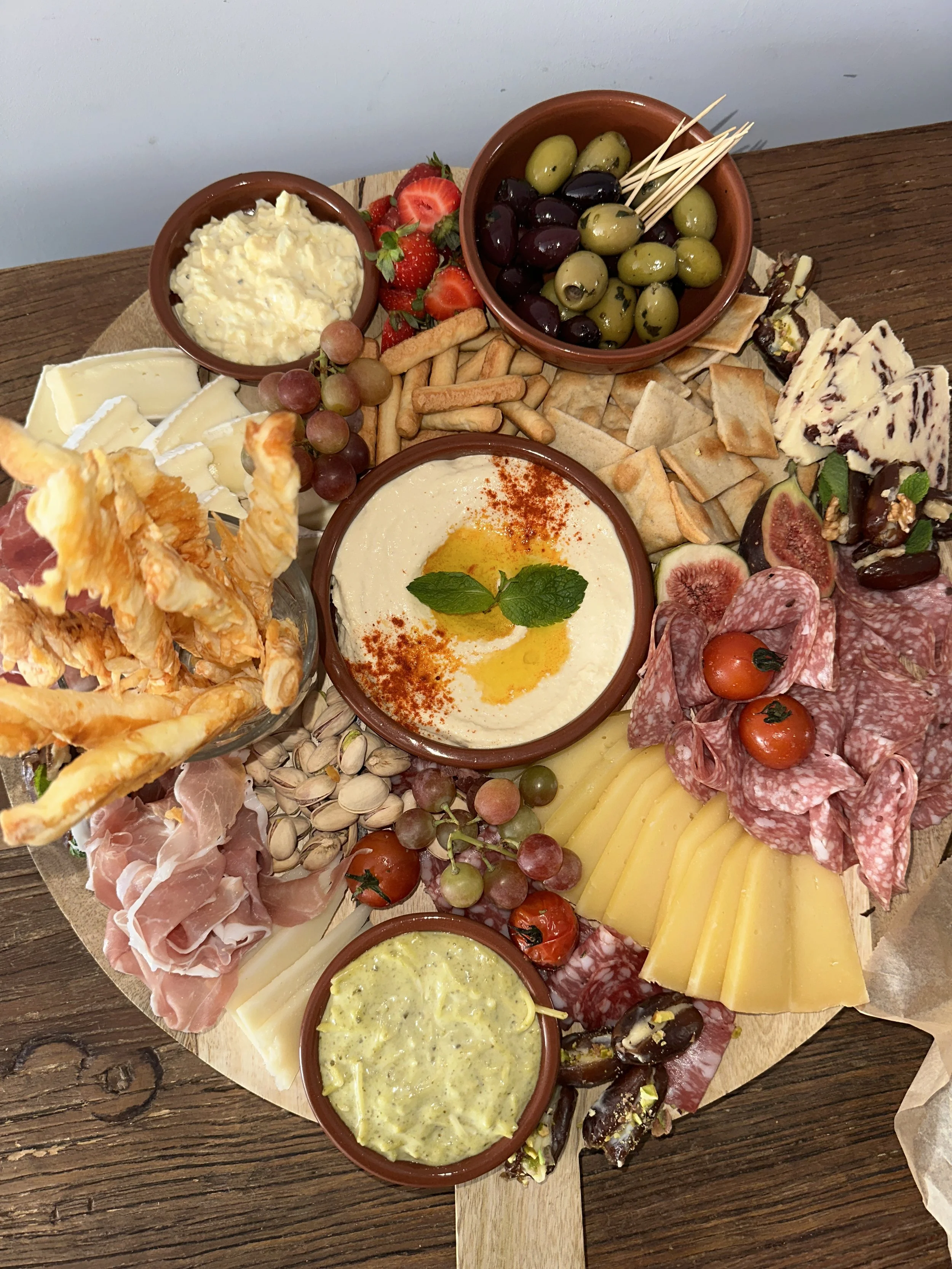 Een brunchplank met diverse kazen, vleeswaren, olijven, dip, fruit, crackers en brood.