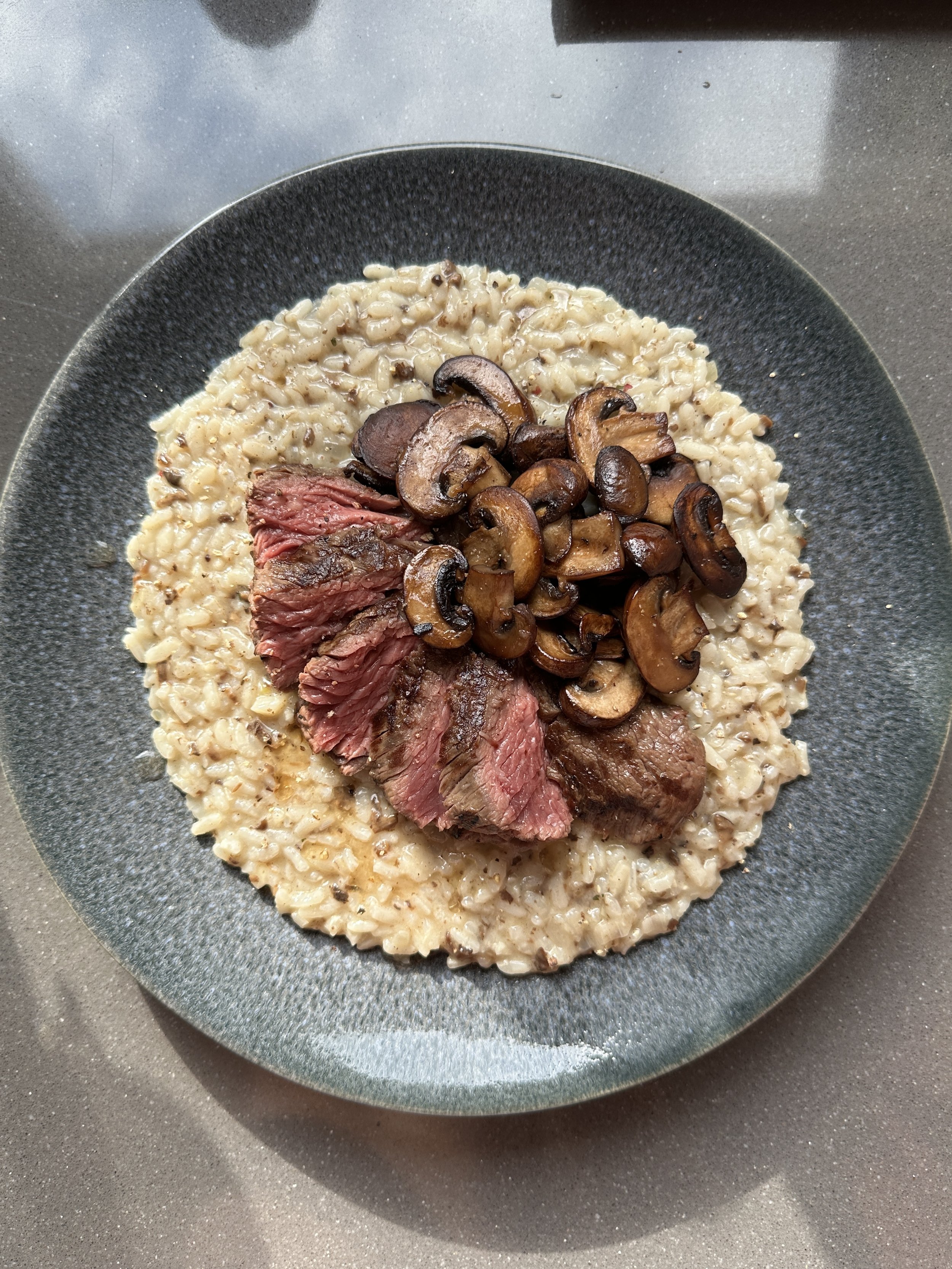 Risotto met steak en gebakken paddestoelen op een zwarte bord.