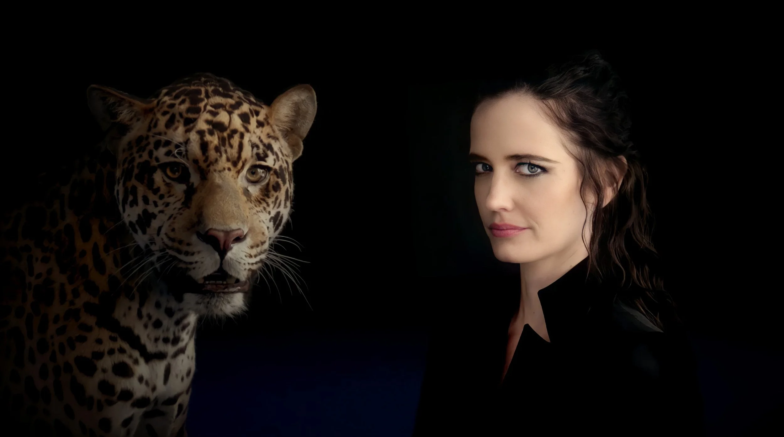 A woman with long dark hair and blue eyes posing with a leopard, both against a black background.