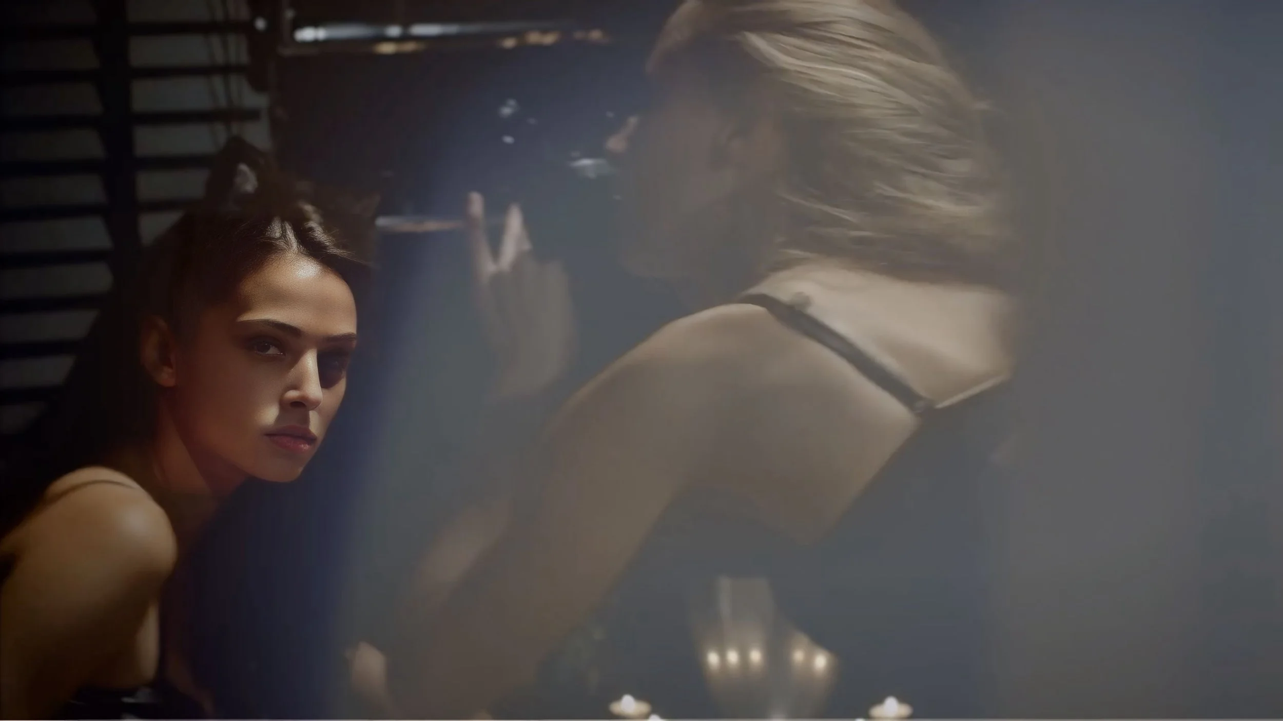 A woman with makeup and styled hair looking at the camera, while her reflection is visible in a mirror.