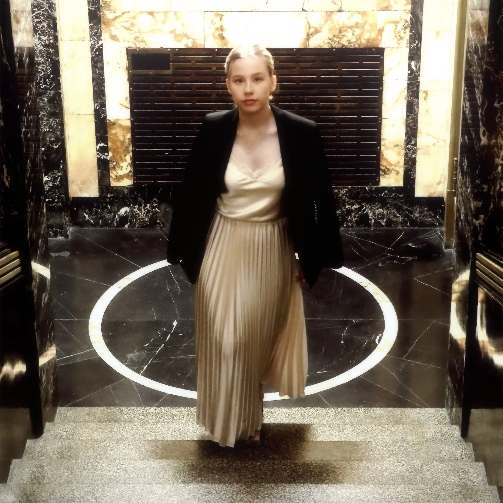 A young woman walking down a staircase in an elegant lobby with black and gold marble walls.