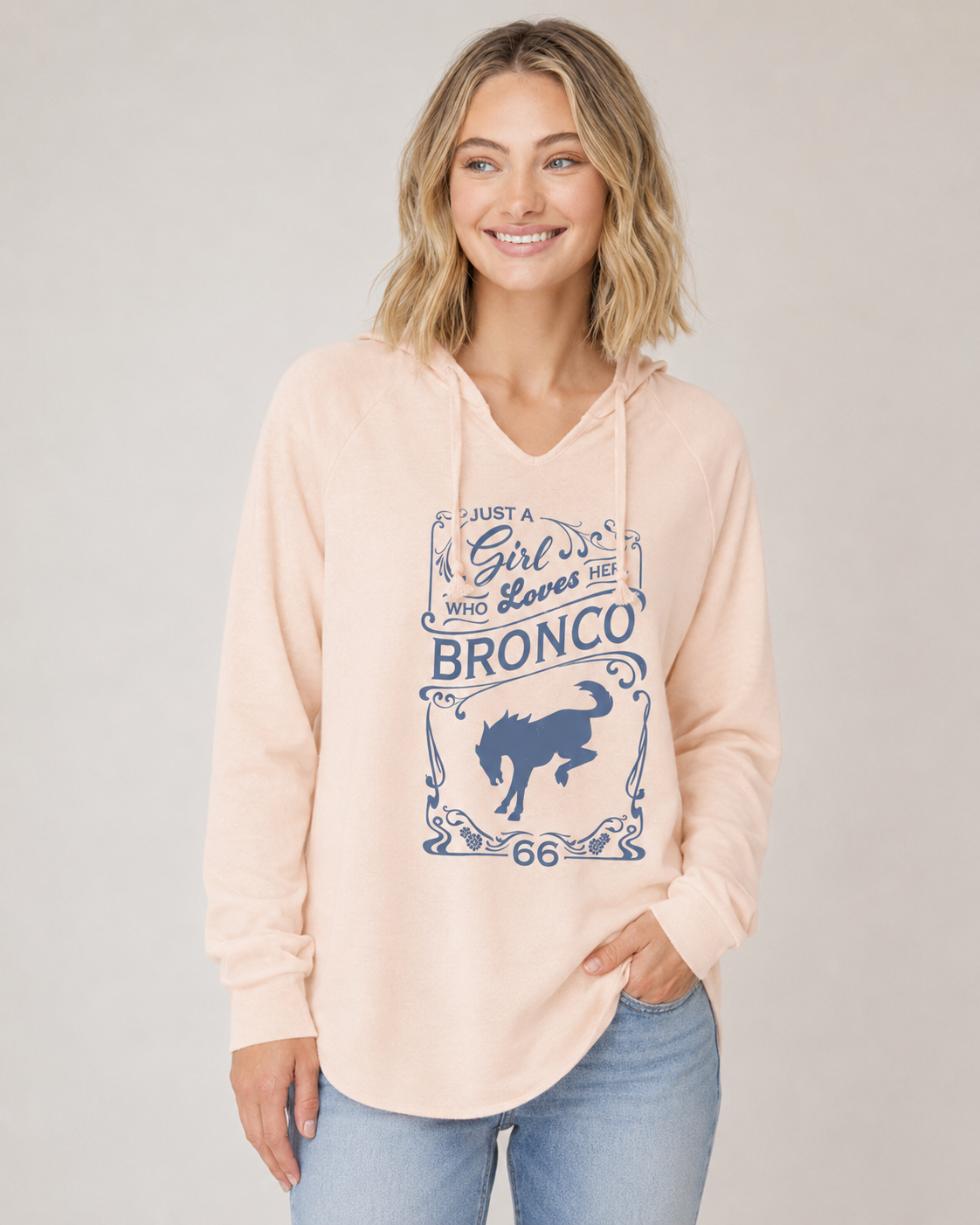 Women's blush pink hooded pullover featuring Just a Girl Who Loves Her Bronco graphic in blue with vintage western typography and bucking horse artwork.