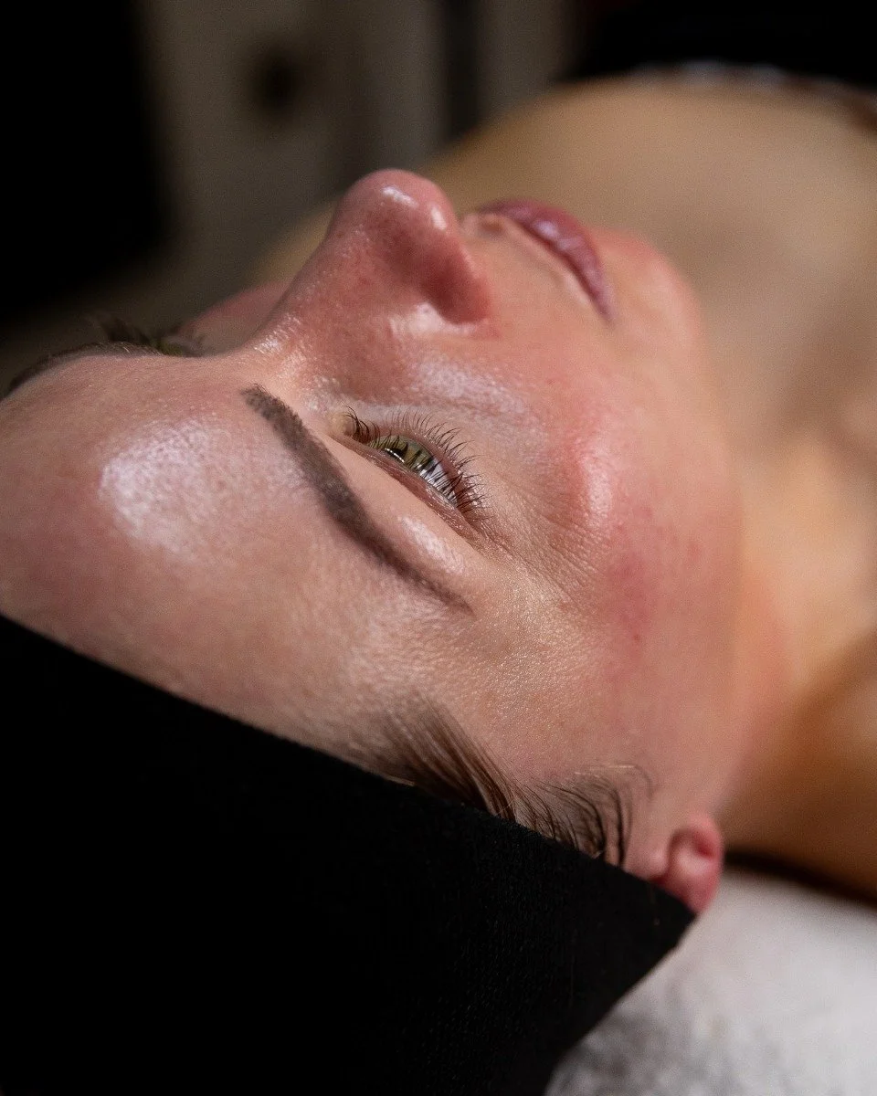 Close-up of a woman's face lying down with her eyes closed, showing her natural skin texture, fine eyelashes, and well-defined eyebrows.