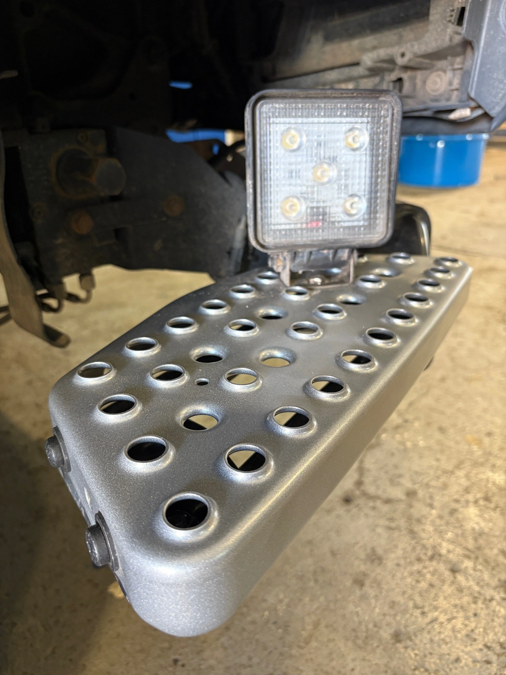 Bodenplatte mit runden Schlitzen unter einem LKW-Fahrzeug, mit einem rechteckigen LED-Reflektor darüber