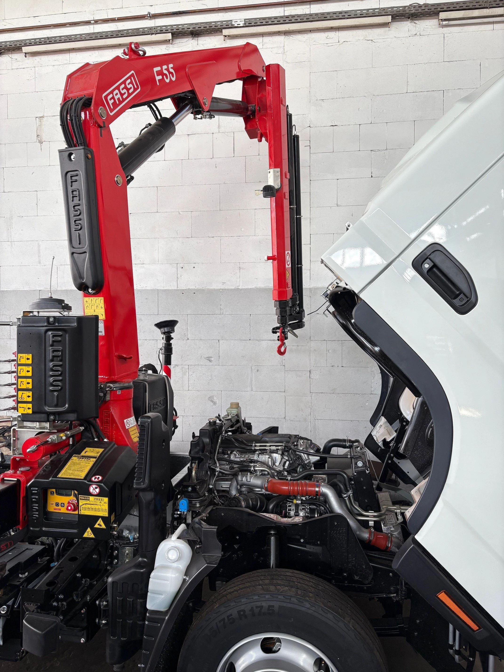 LKW mit deaktivierter Motorhaube und einem Roten Kran im Inneren eines Garagen- oder Werkstattbereichs.