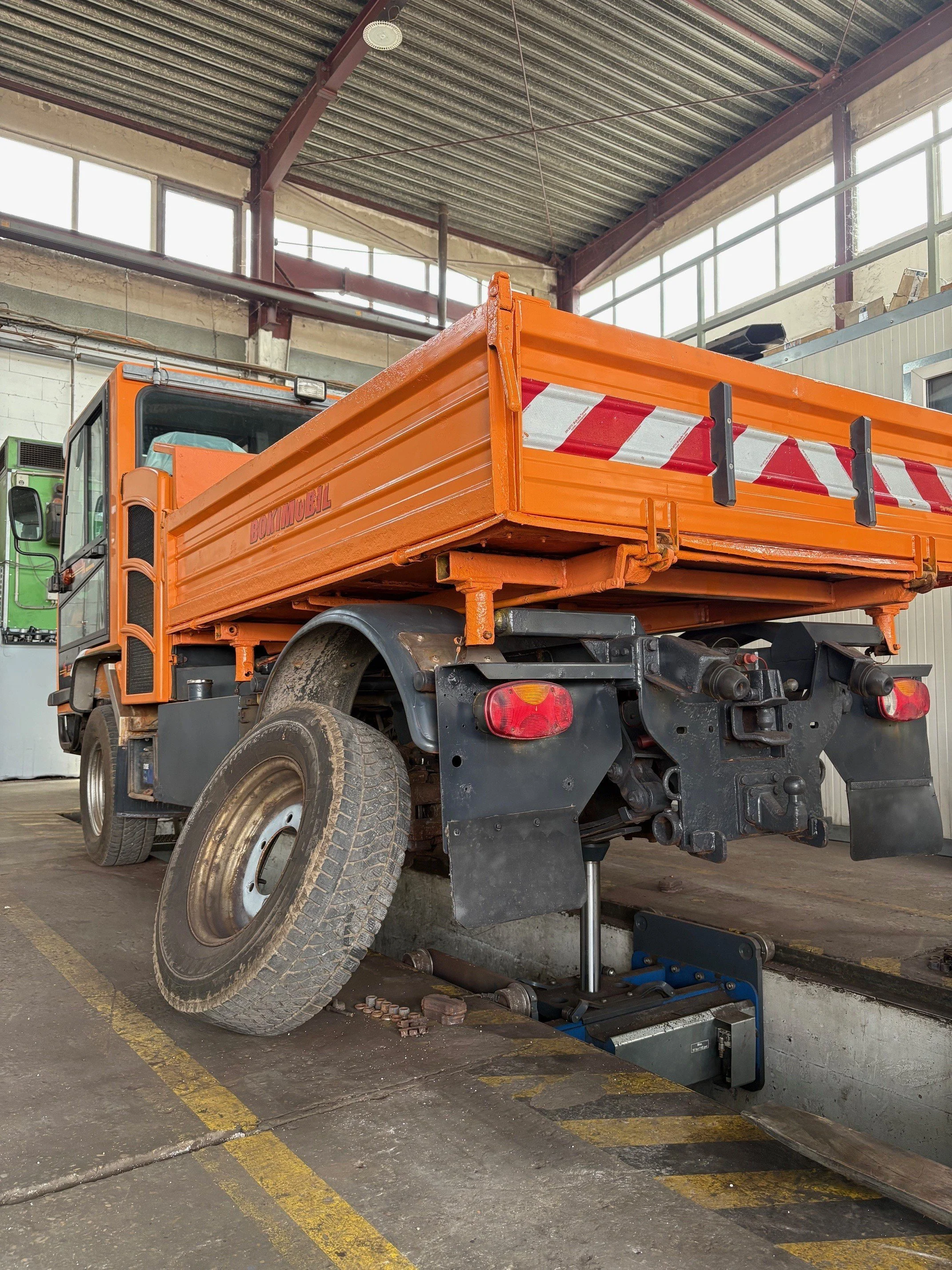 Ein orangefarbener Bauwagen in einer Werkstatt, auf einer Hebebühne, die im Boden versenkt ist.