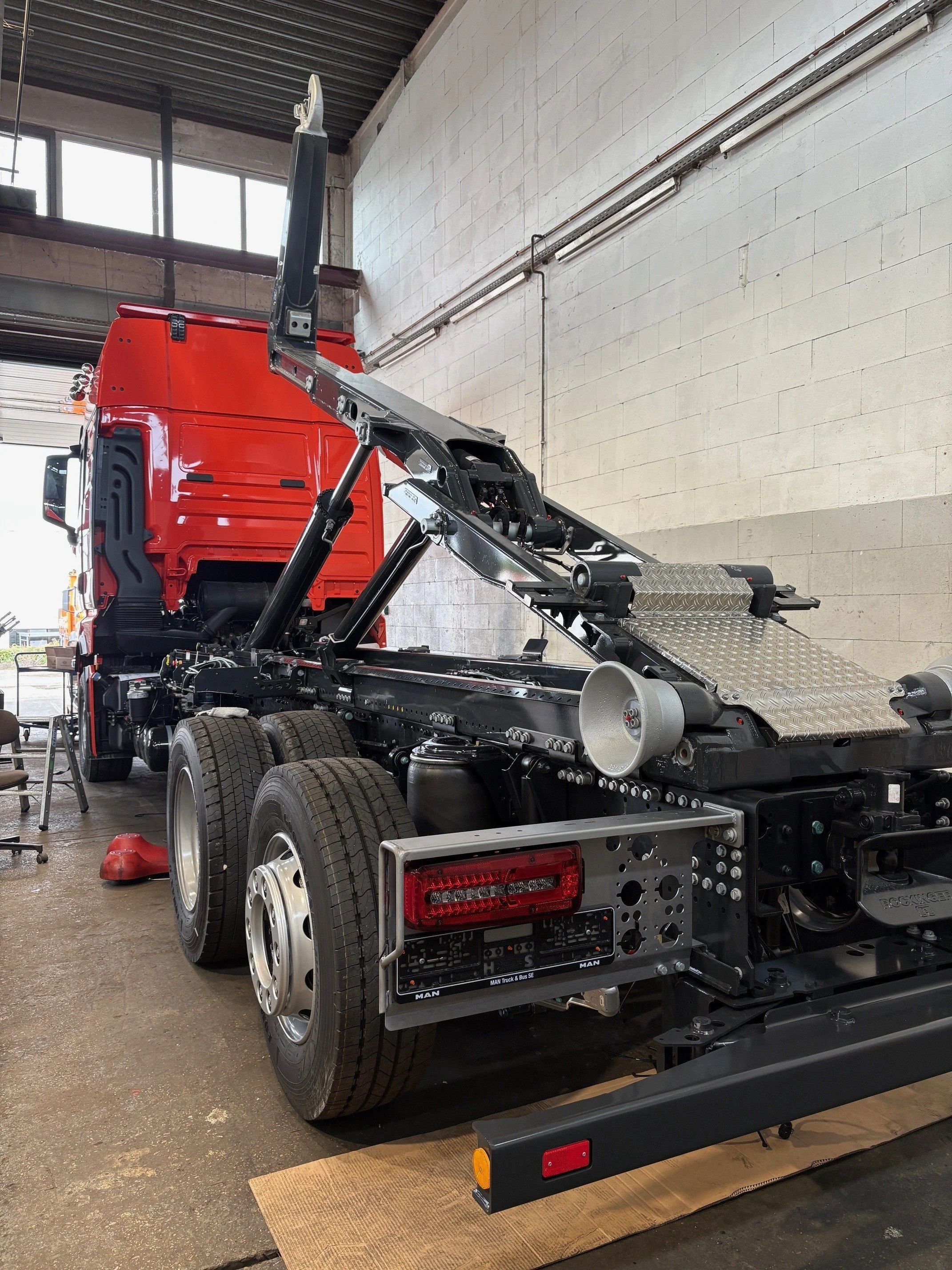 Ein unmontiertes LKW-Chassis mit rotem Fahrerhaus in einer Werkstatt.