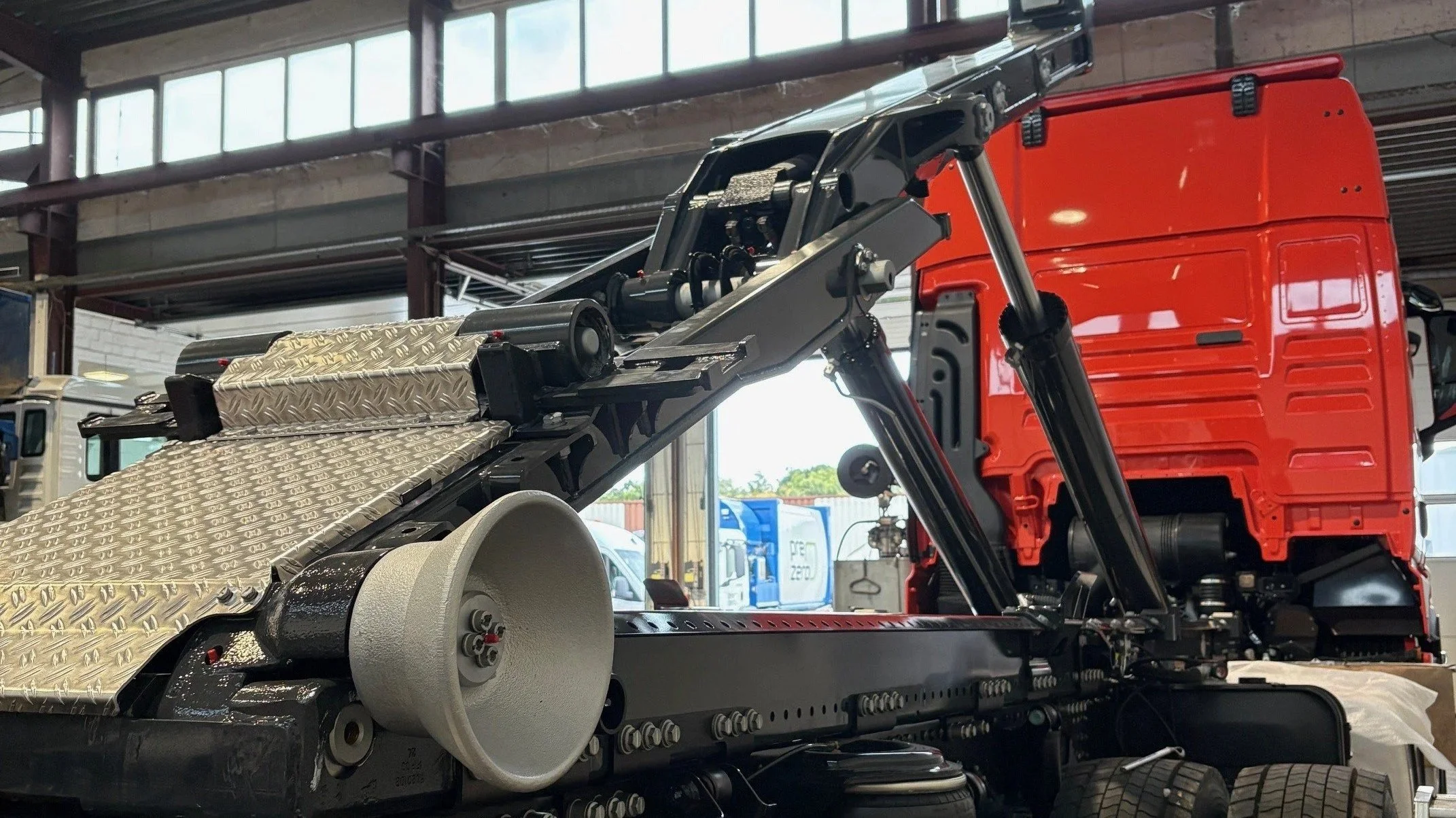 Nahaufnahme eines Lastwagenrahmens mit Hebevorrichtung bzw. Kipphydraulik und Werkzeugen im Werkstattinneren.