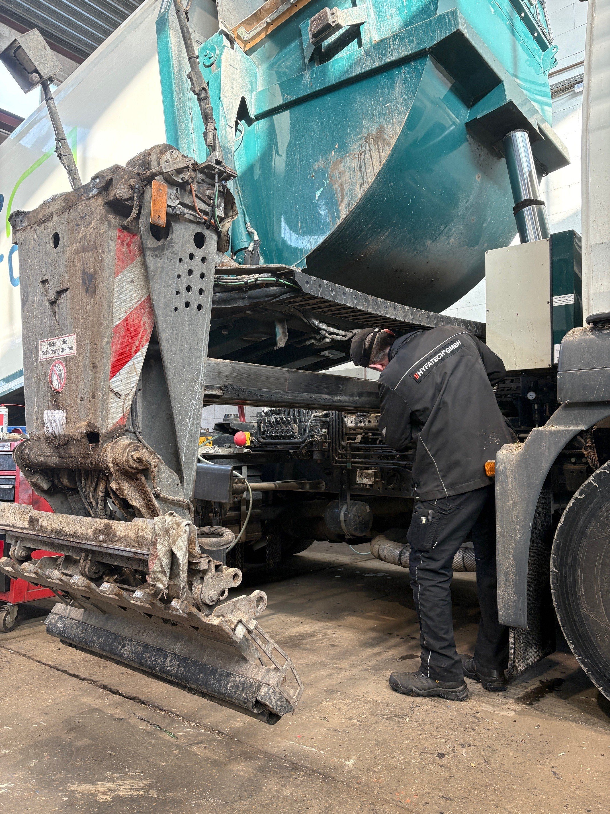 Ein Techniker arbeitet an einem großen Lastwagen, offenbar bei Wartungs- oder Reparaturarbeiten in einer Werkstatt.