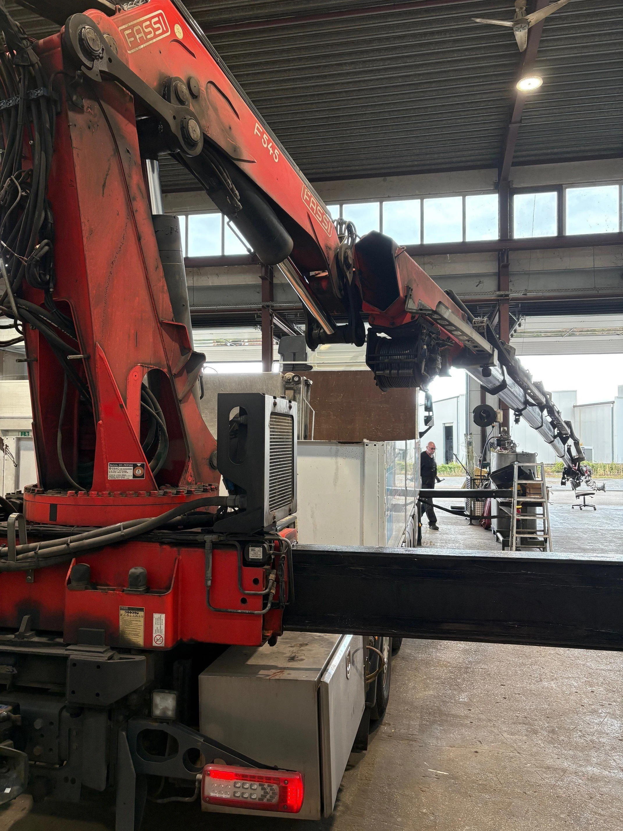 Ein großer, roter Kran im Inneren einer Halle, mit ausgestrecktem Ausleger und Arbeitsplattform im Hintergrund.