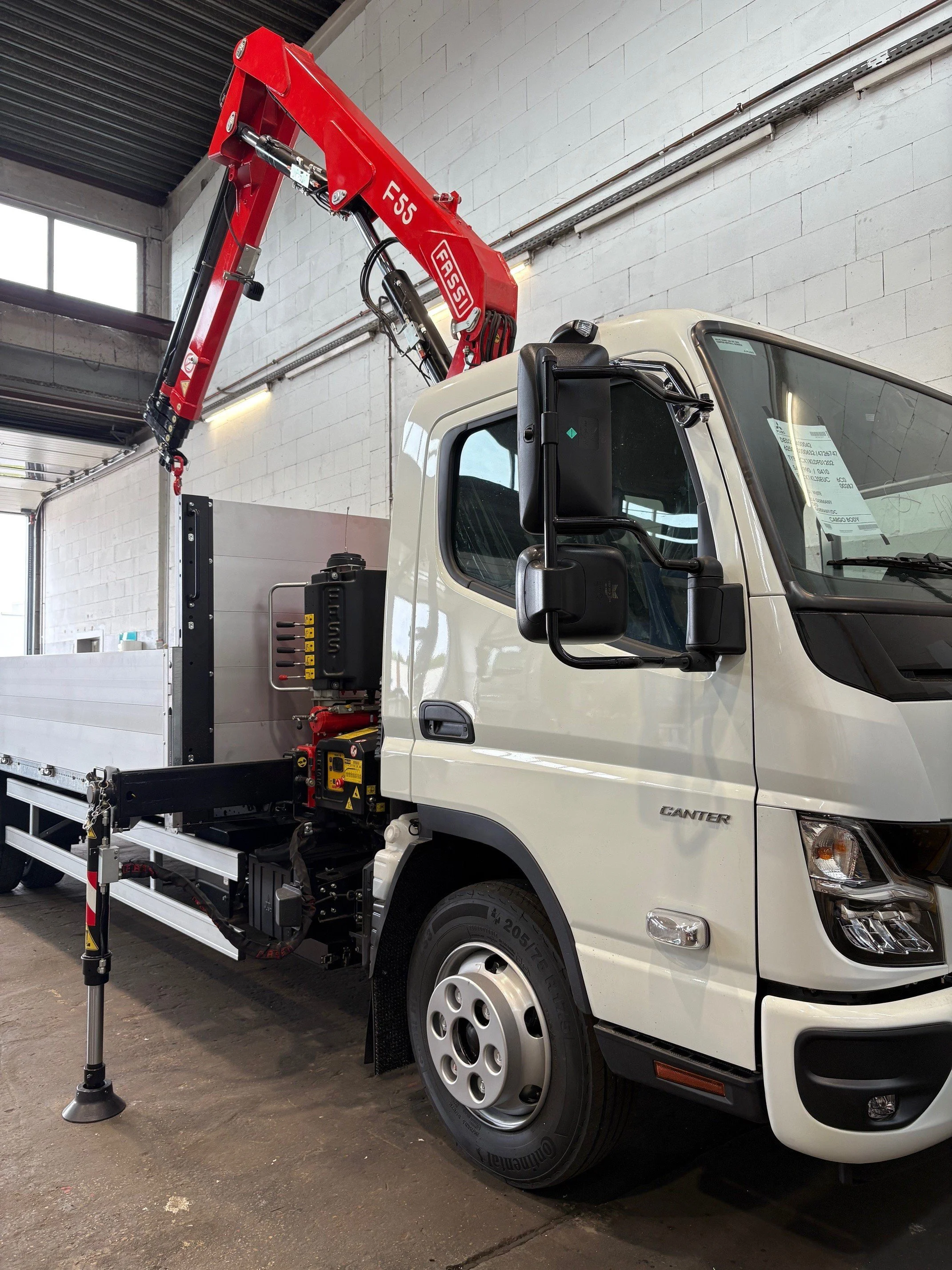 Weißer Lieferwagen mit rotarmigem Kran auf einem Industrieparkplatz.