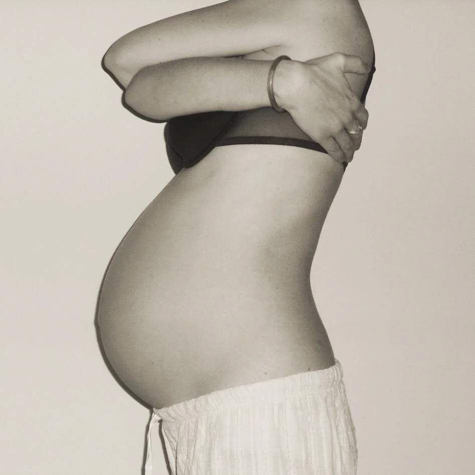 Side view of a pregnant woman with arms crossed over her chest, wearing a sports bra and loose shorts.